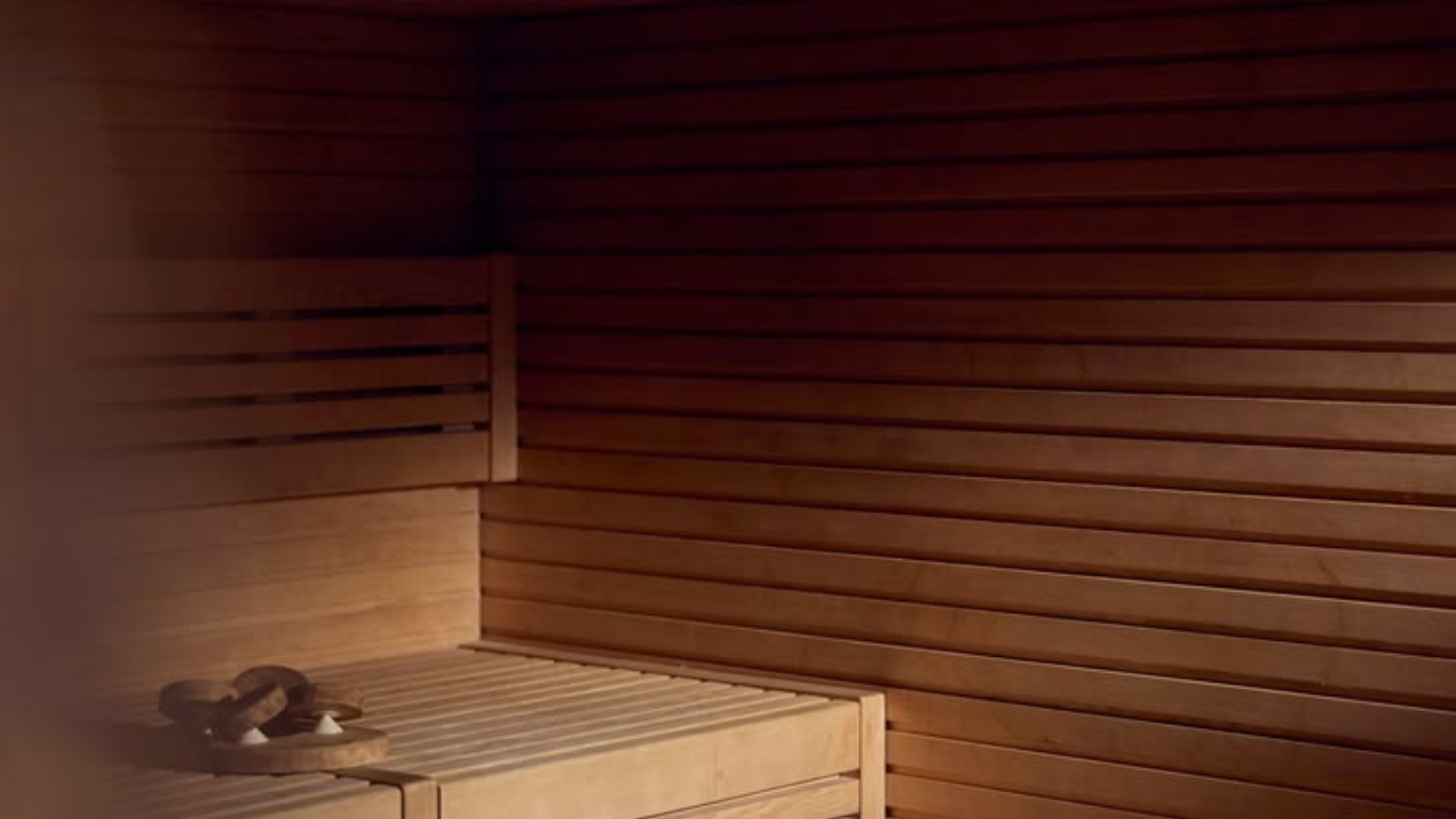 Empty wooden sauna with benches and slippers on the lower bench.
