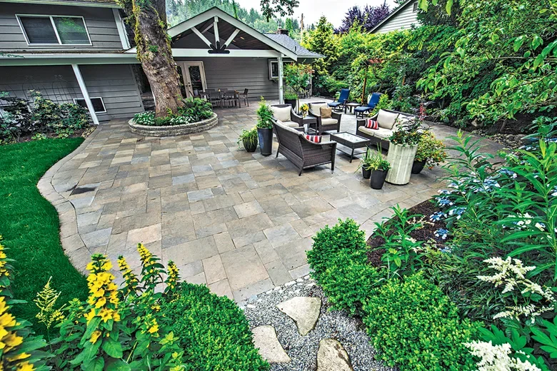Backyard patio with outdoor seating, potted plants, and lush greenery surrounding a small house.