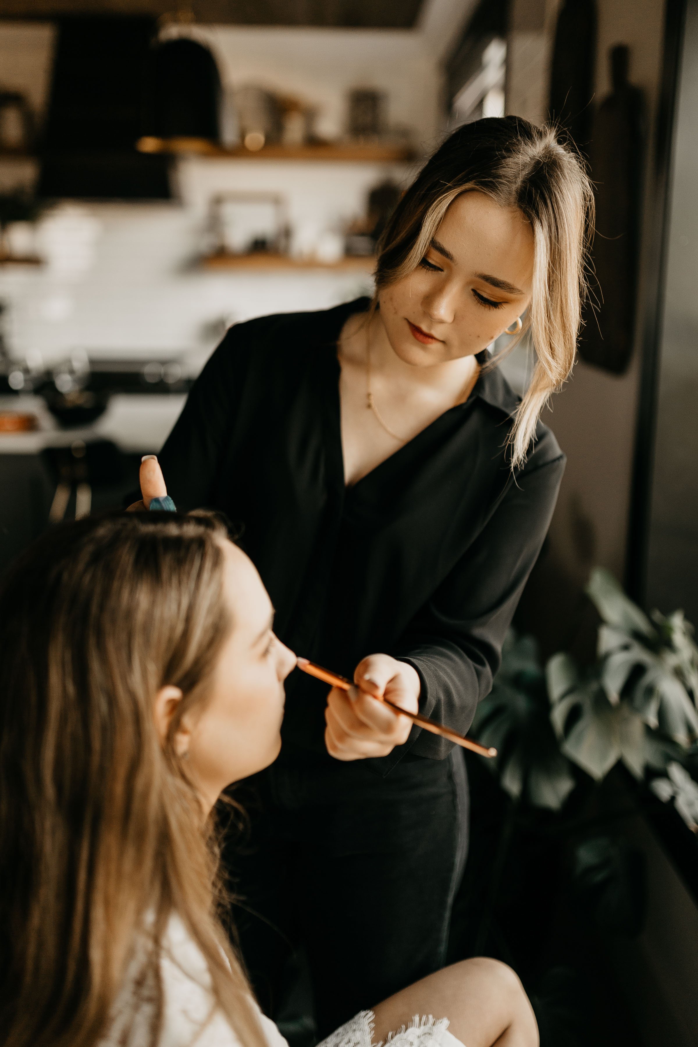 A woman applying makeup to another woman in a cozy indoor setting.