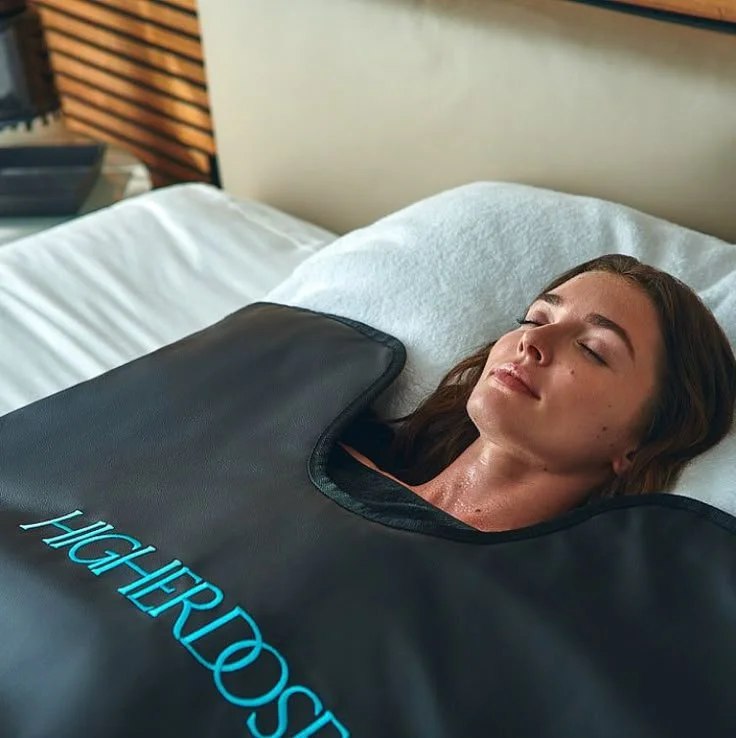 A woman lying in bed with a black harness around her neck that says 'HYPERROSE' and appears to be a cooling or relief device. She has her eyes closed and looks relaxed.