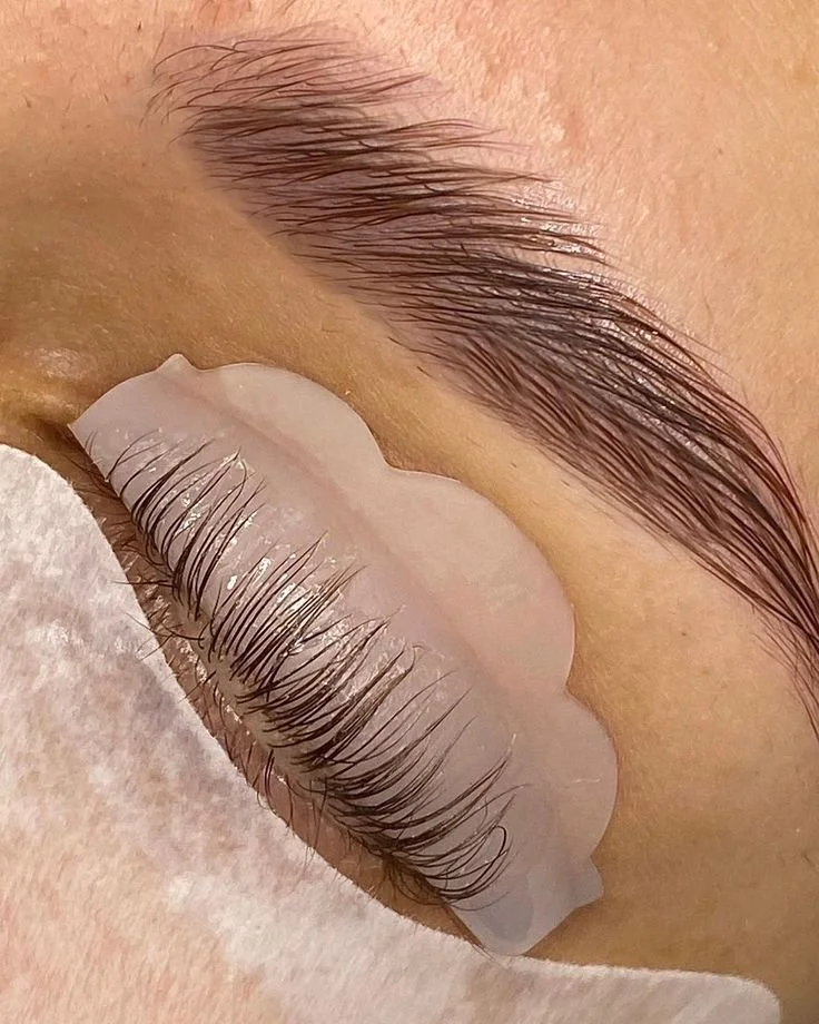 Close-up of a person's closed eye, showing well-groomed eyebrow and long, curled eyelashes, with a white protective patch over the lower lashes.