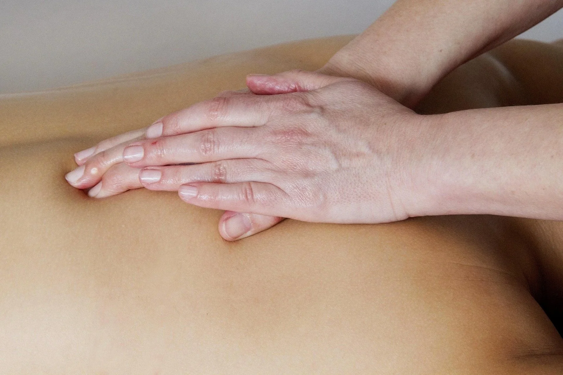 Close-up of a massage therapist's hands giving a massage to a person's back, which has smooth, tan skin.
