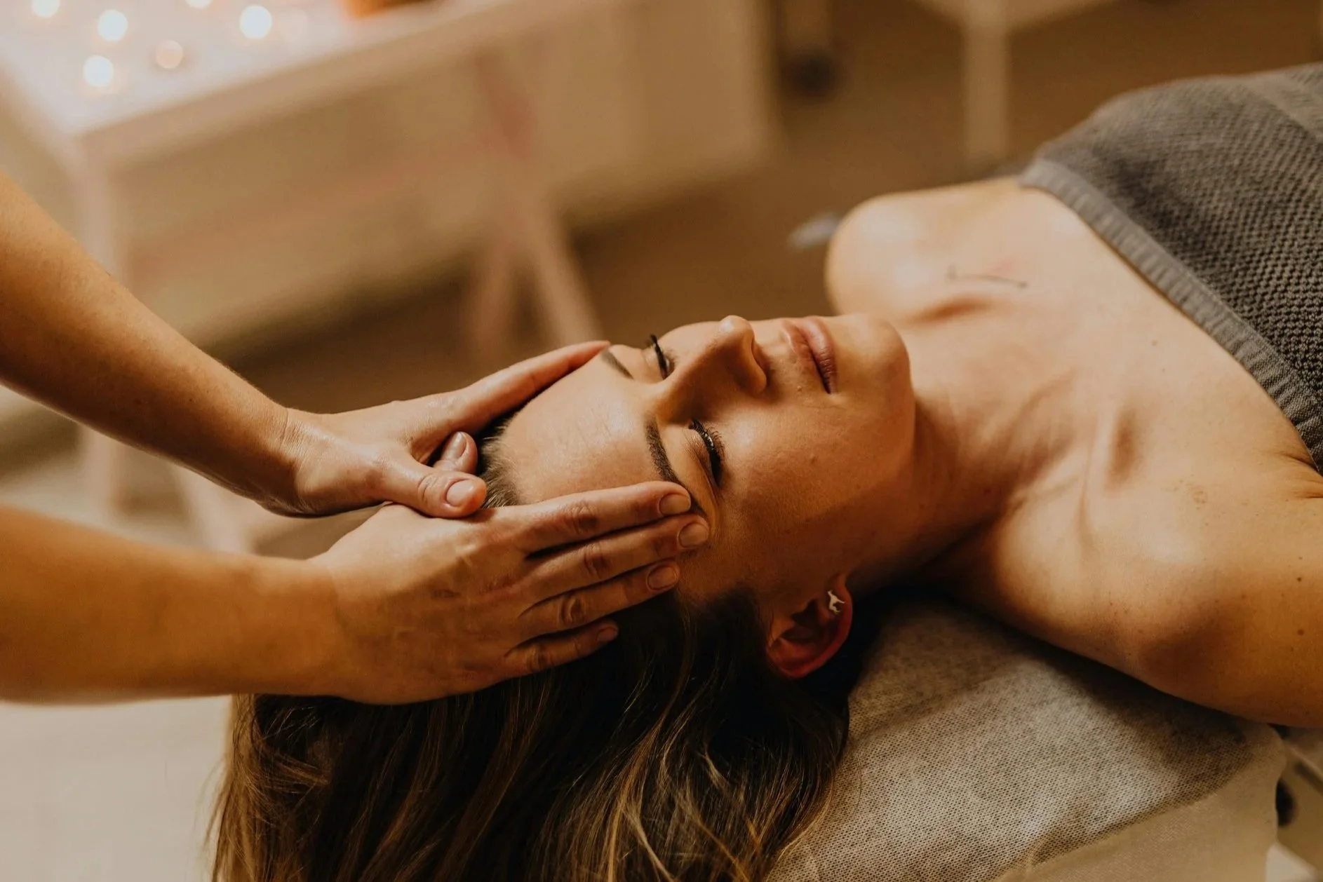 A woman receiving a facial massage while lying on a treatment table.