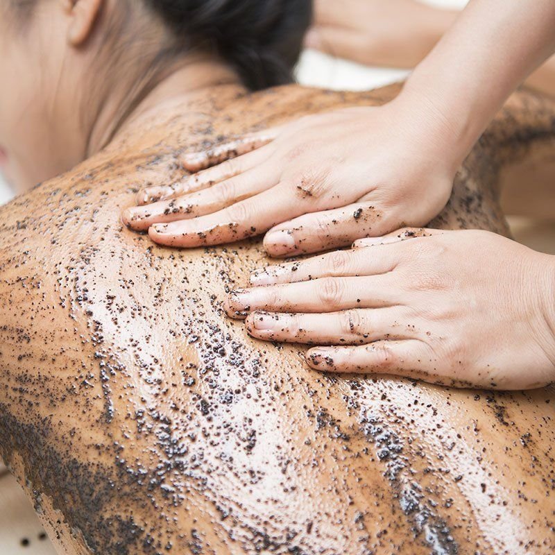 Person receiving a back scrub or massage with black exfoliating particles on their skin, while lying face down.
