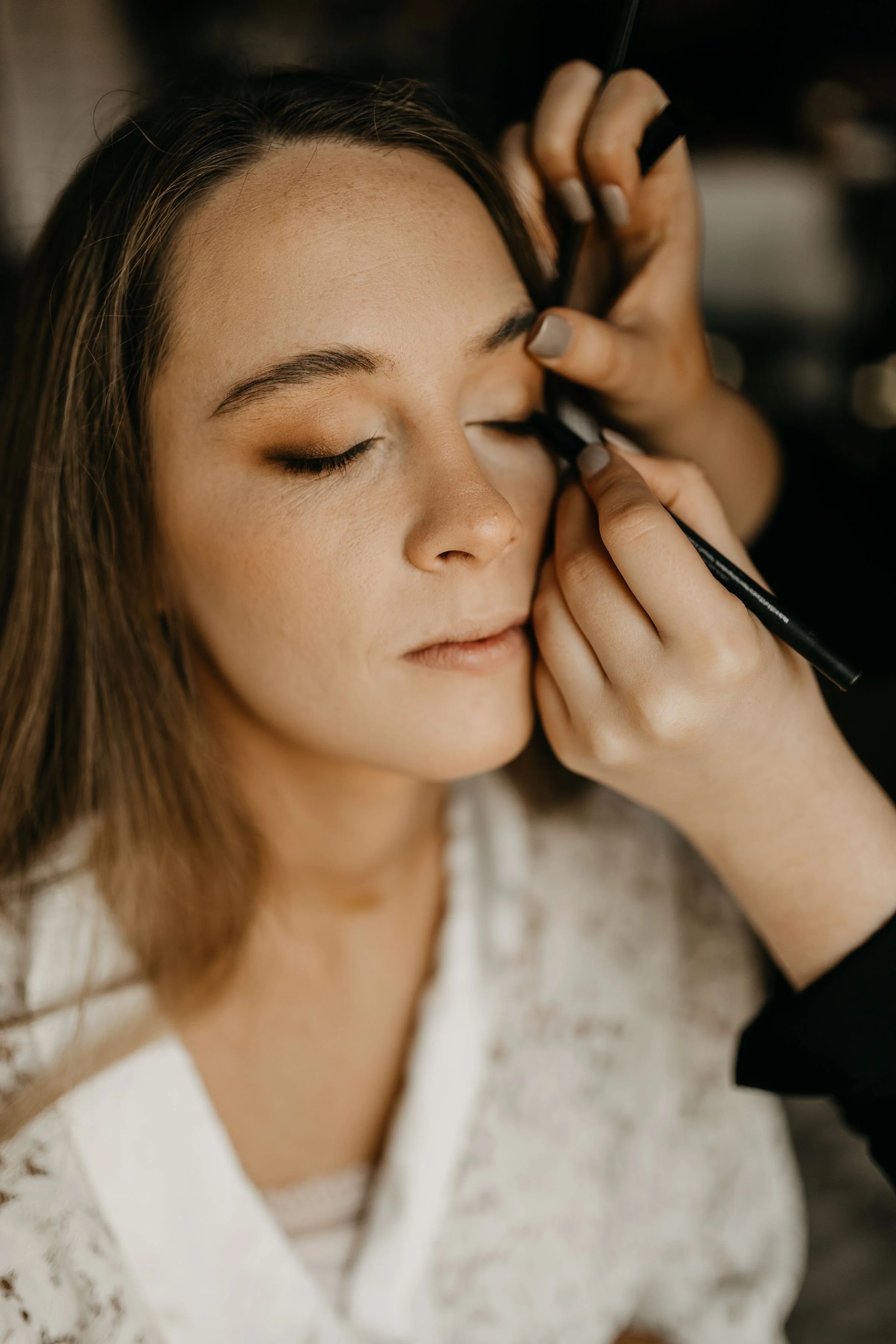 A woman has her makeup done as a makeup artist applies eyeshadow with a brush.