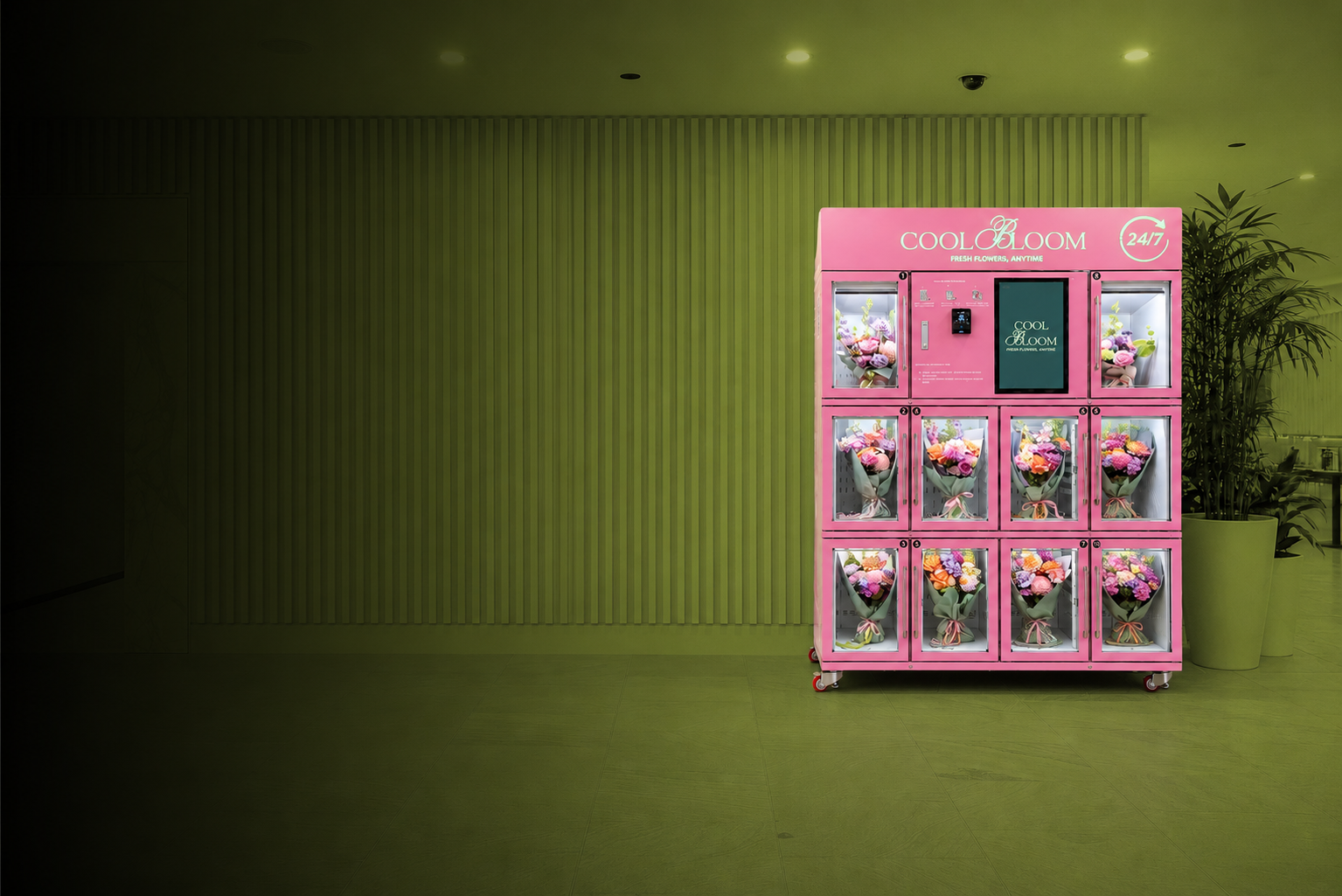 Pink floral vending machine with bouquets of flowers inside, located in a public indoor space with green walls and potted plants.