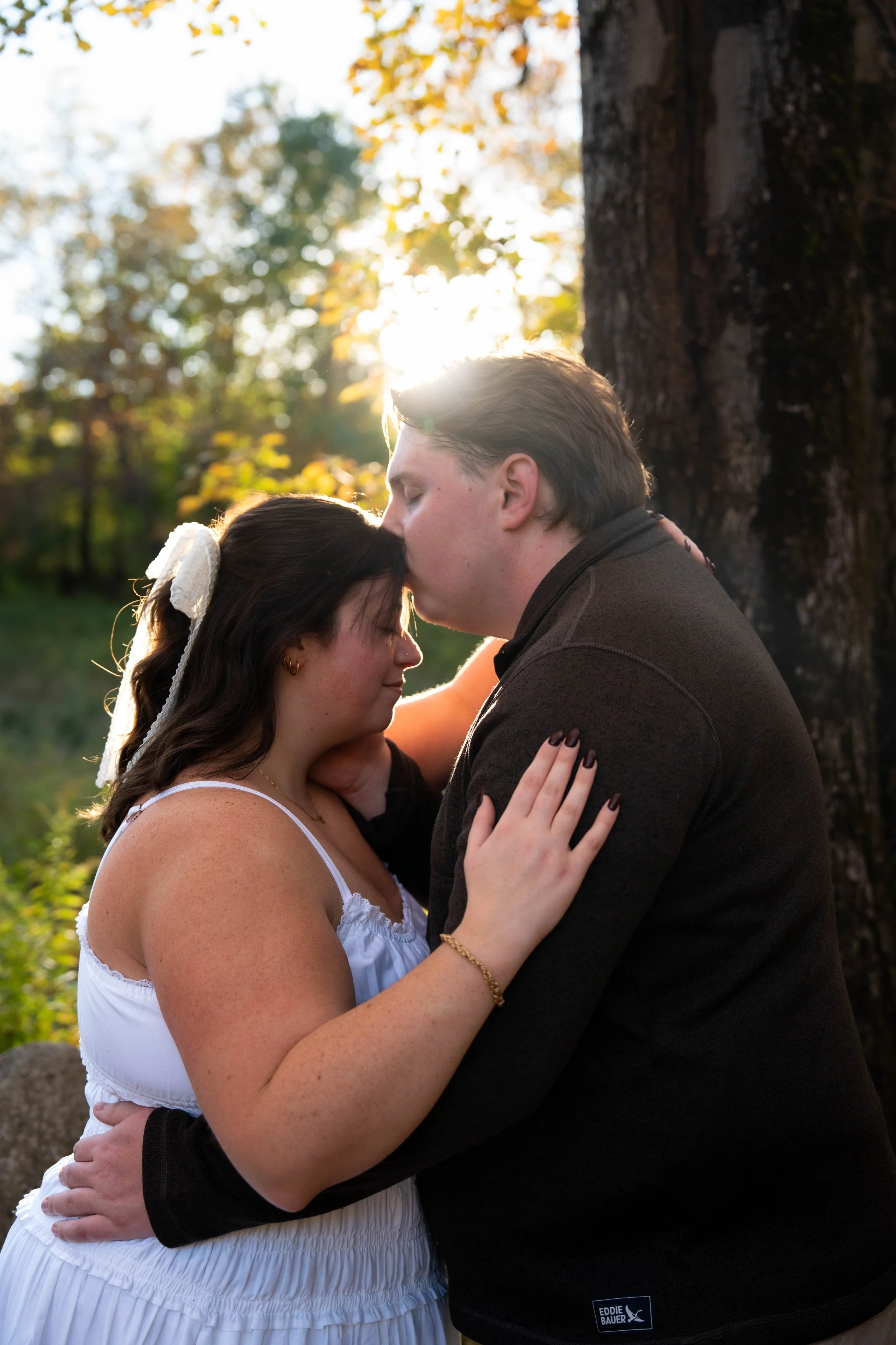 Couple embracing outdoors in autumn sunlight beside a tree