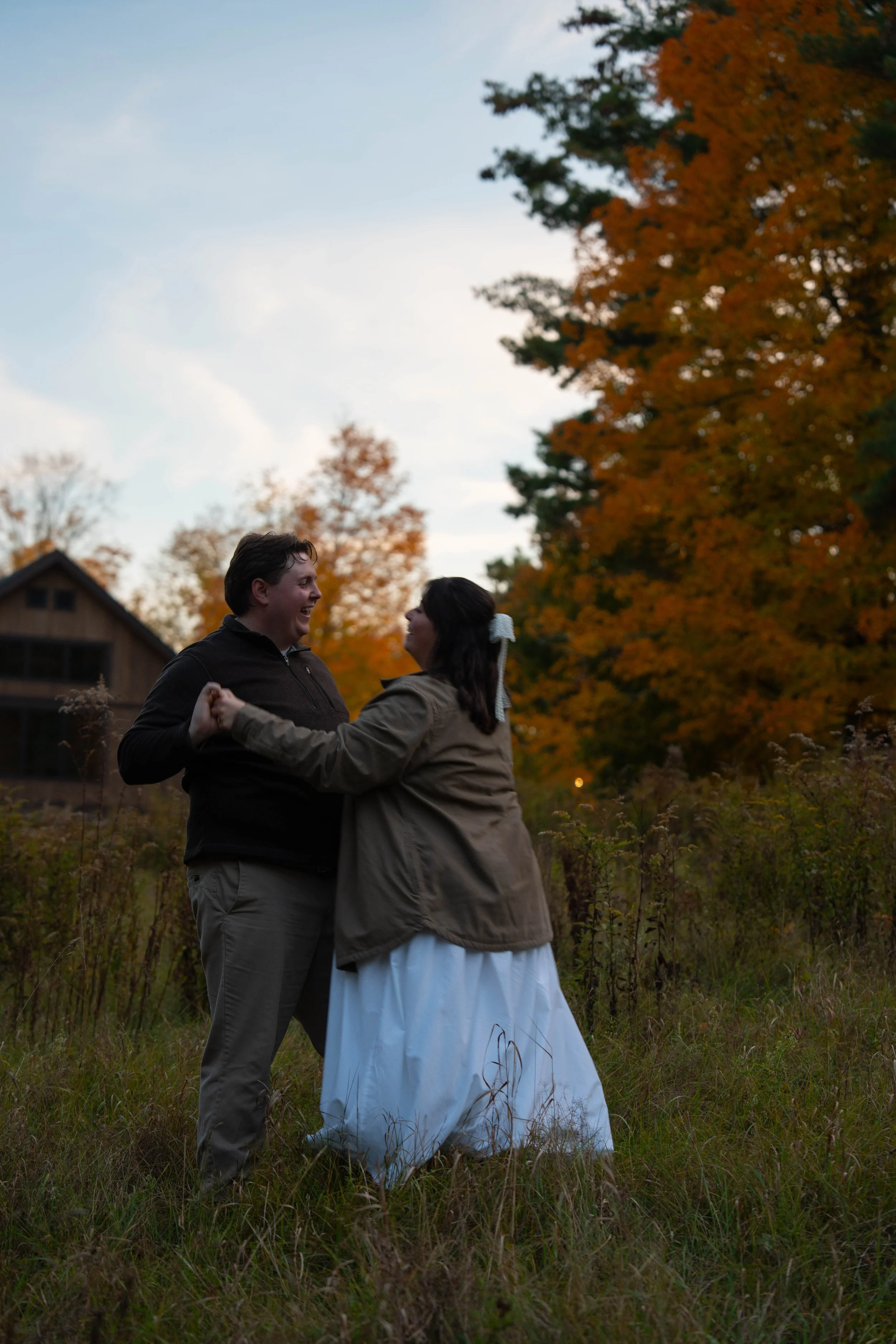Couple dancing in a grassy field surrounded by autumn trees