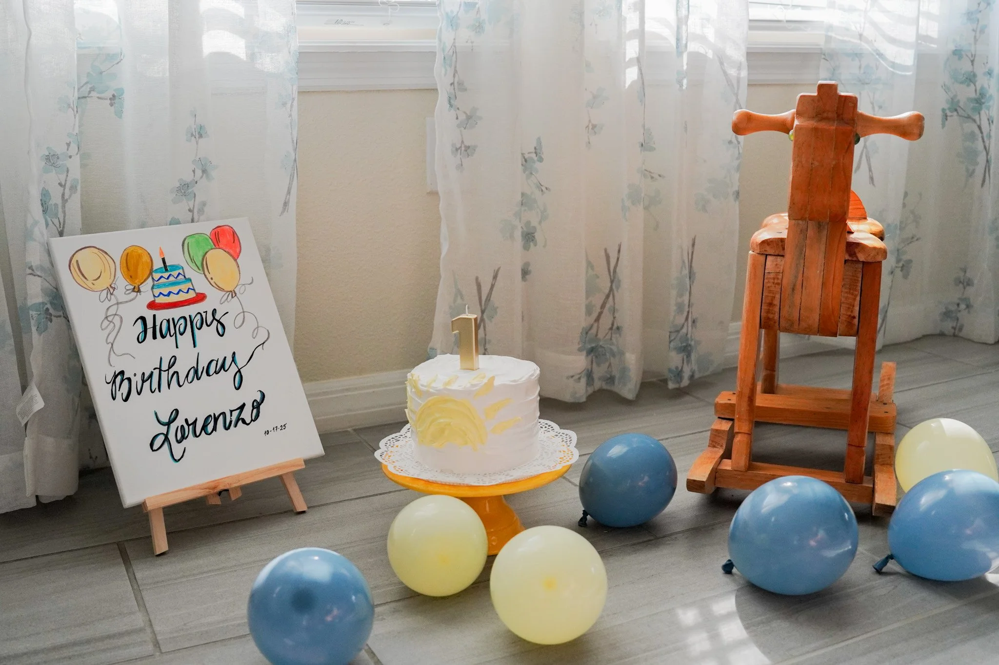 Birthday party setup with a decorated cake, balloons, a birthday sign for Lorenzo, and a wooden rocking horse.
