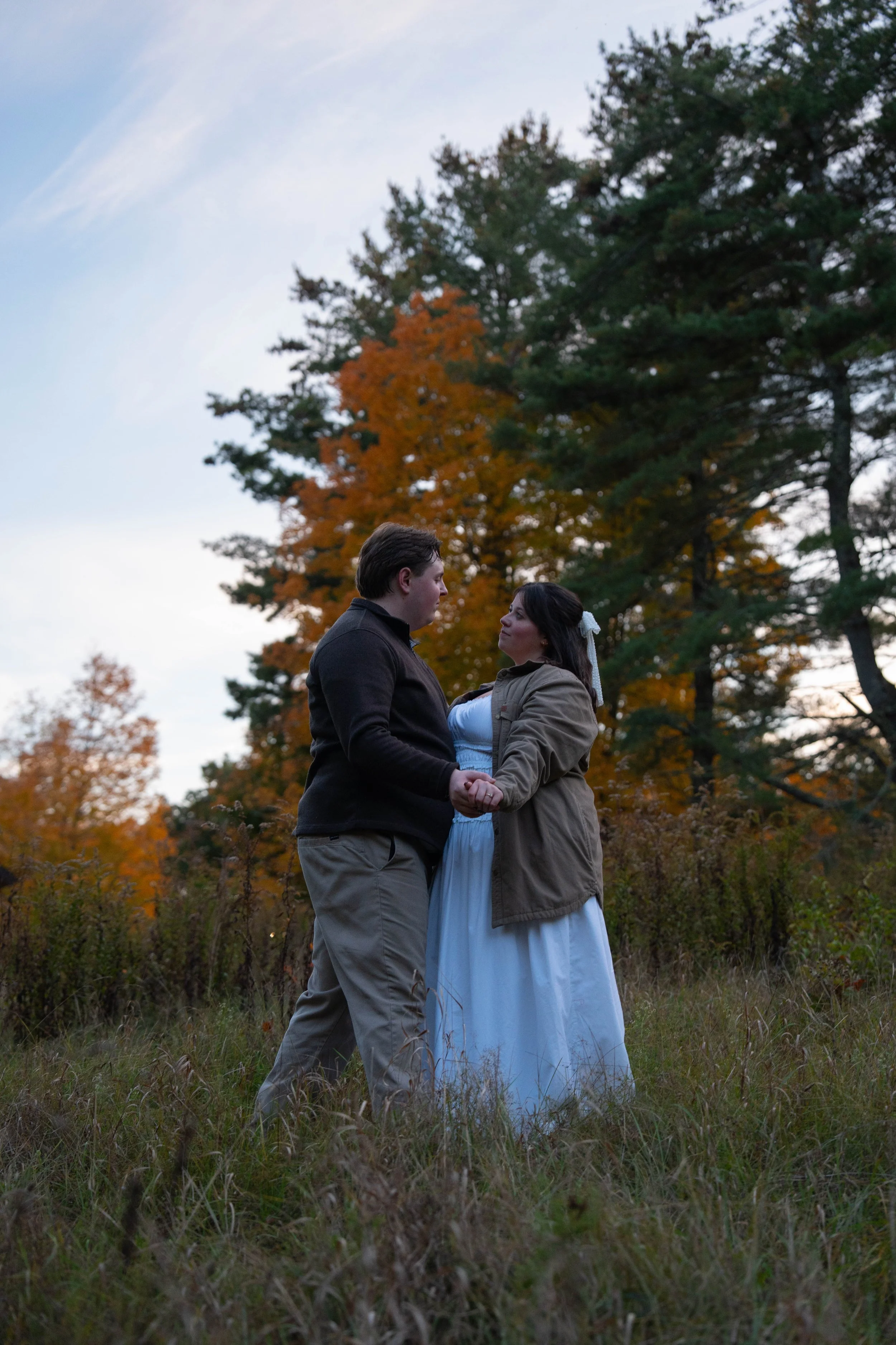 Couple holding hands in a grassy field surrounded by autumn trees