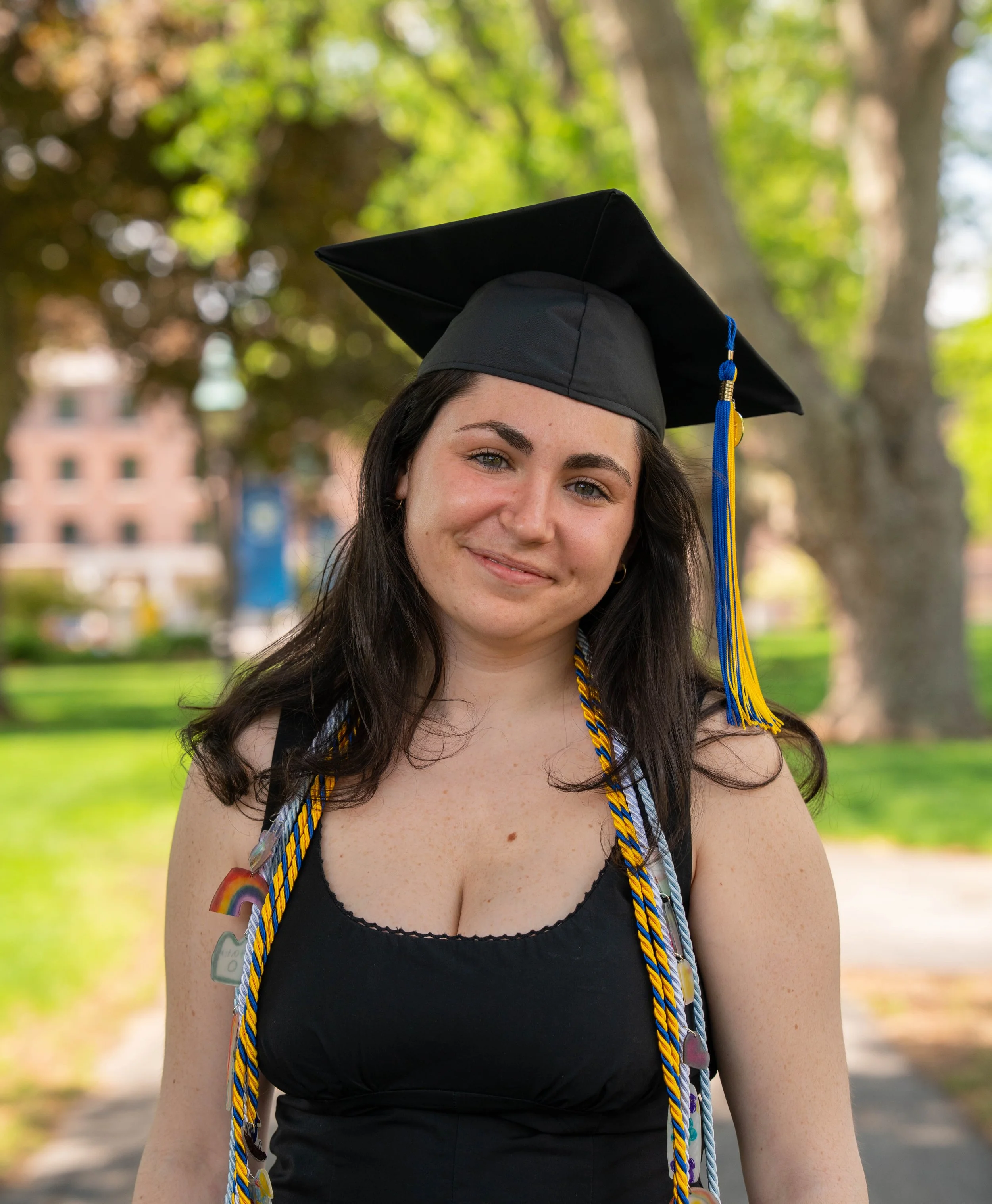 Smiling graduate wearing a black cap and gown with blue and gold honor cords outdoors