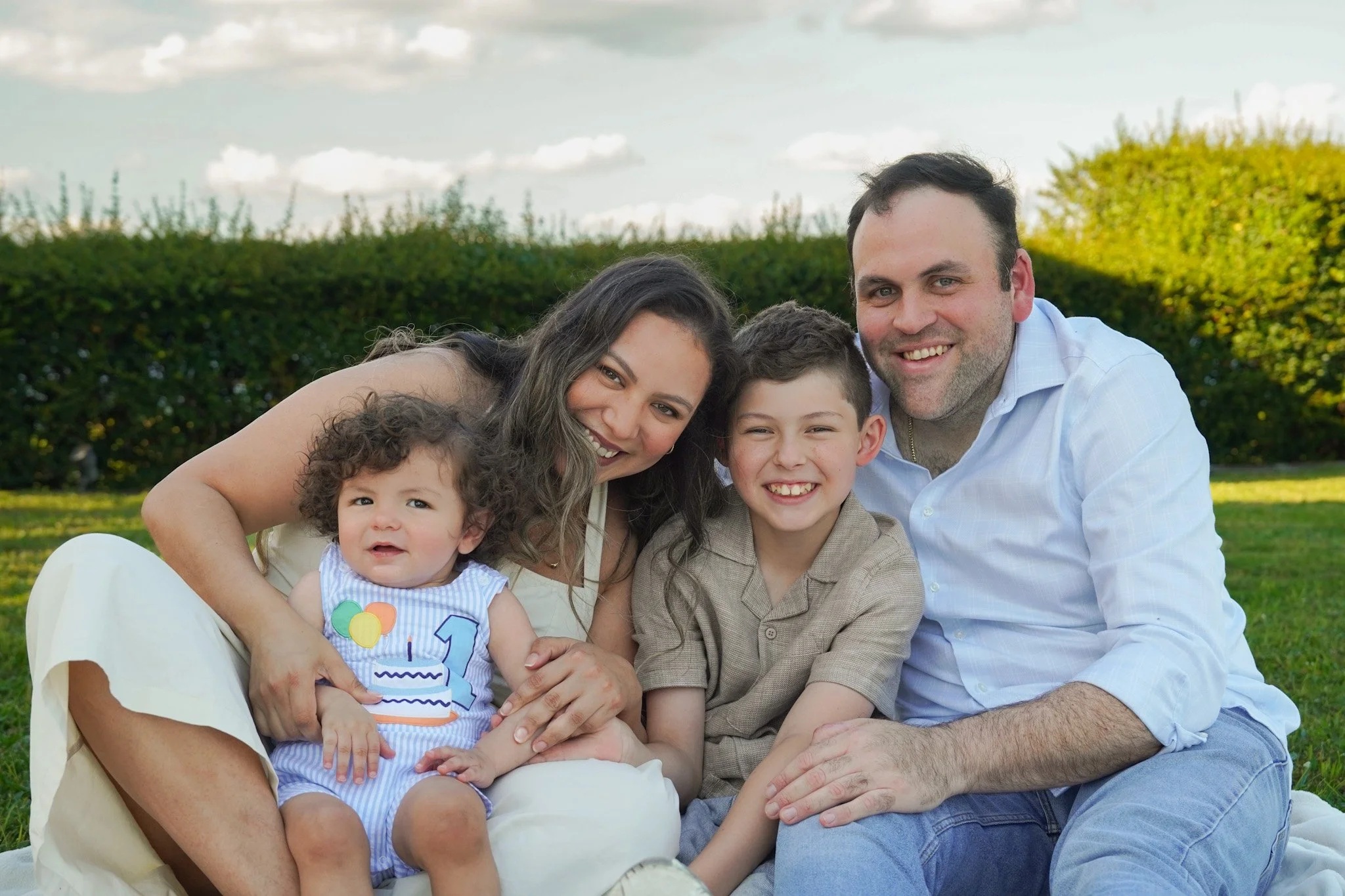 Smiling family of four posing together on a lawn outdoors