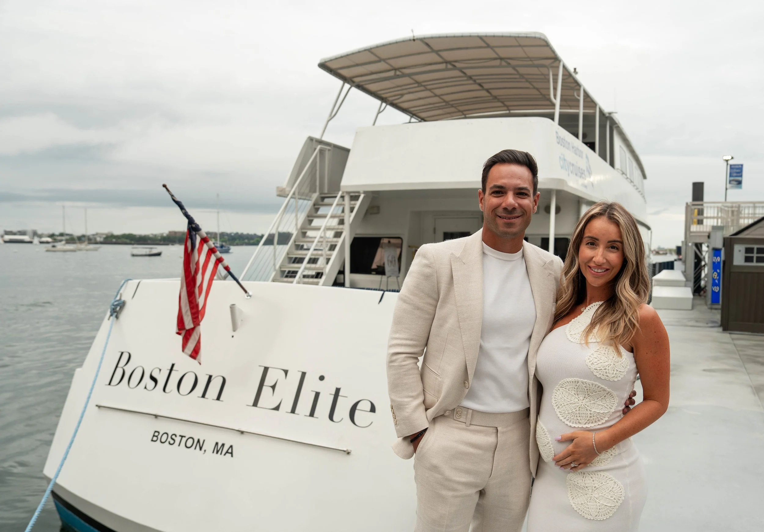 Couple posing aboard the Boston Elite yacht in Boston Harbor, Massachusetts, beside an American flag.