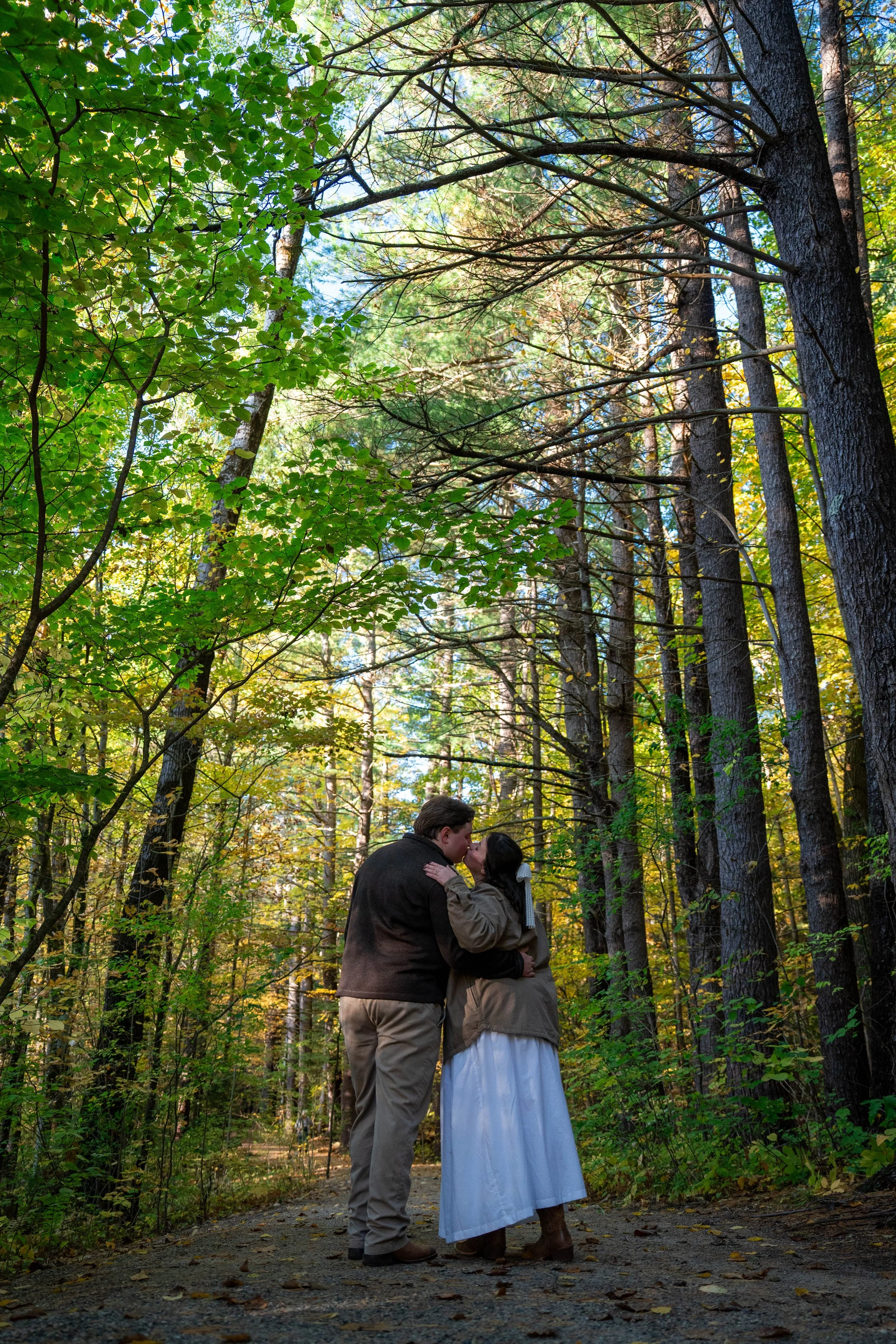 Couple kissing on a wooded forest trail surrounded by autumn trees