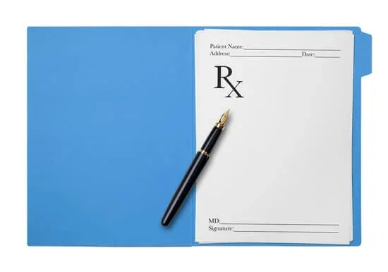 Prescription pad with a pen resting on it against a light blue background.