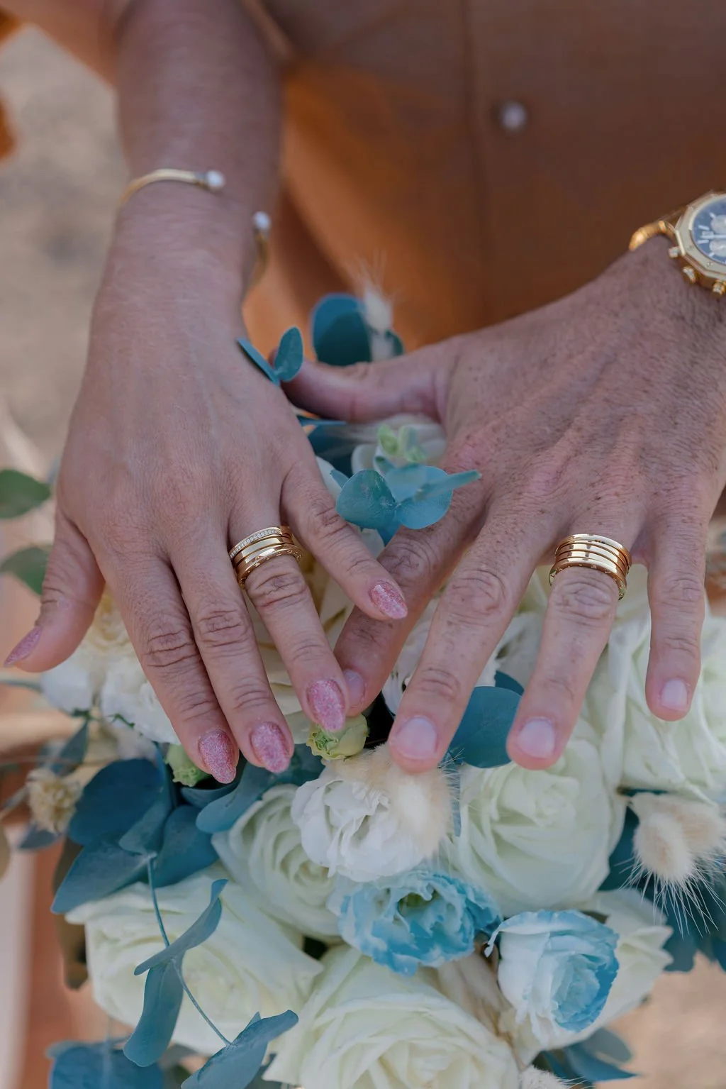 Close-up of two hands with wedding rings, resting on a bouquet of white and light blue flowers with greenery. Just after the elopement ceremony in Santorini