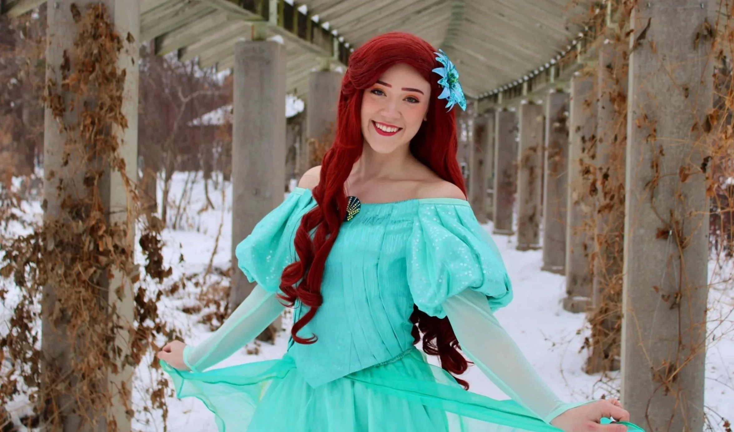 Princess Ariel dressed in a turquoise gown with long gloves, twirling outside in the snow.