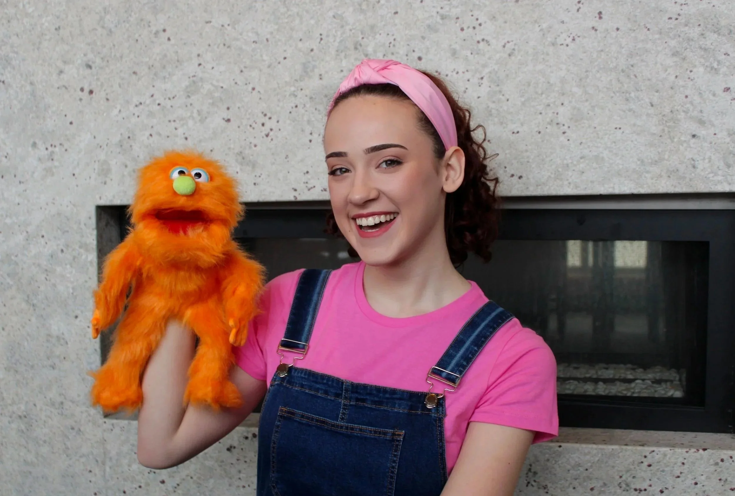 Miss Rach smiling and holding an orange furry puppet with googly eyes.