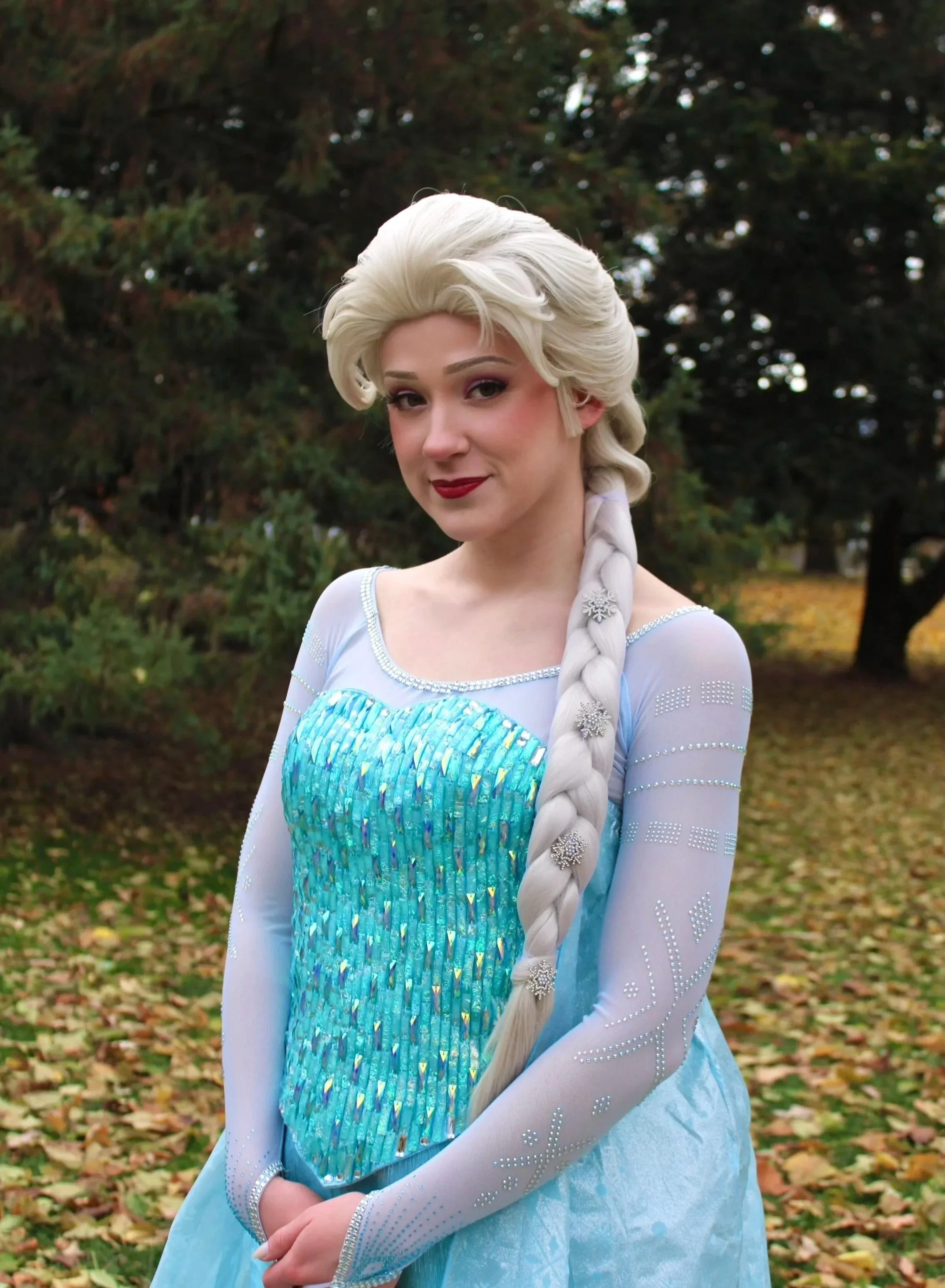 Elsa standing outdoors amidst fallen leaves and trees.