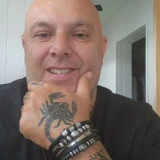 Close-up of a man smiling with a tattoo of a scorpion on his hand, wearing multiple bracelets