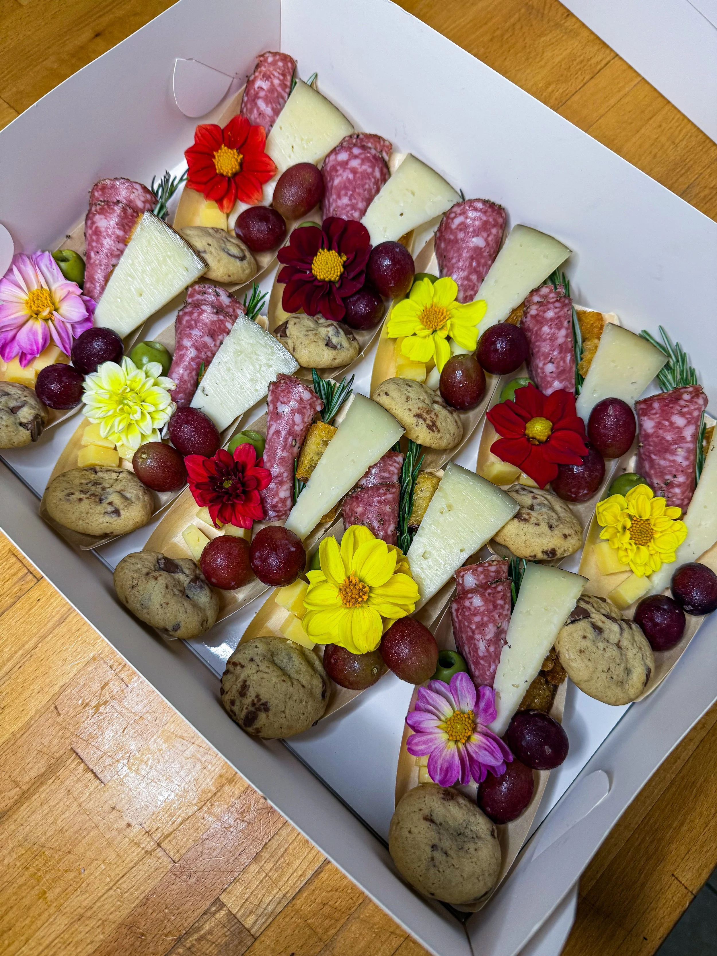 Cheese and charcuterie platter decorated with edible flowers, grapes, and cookies