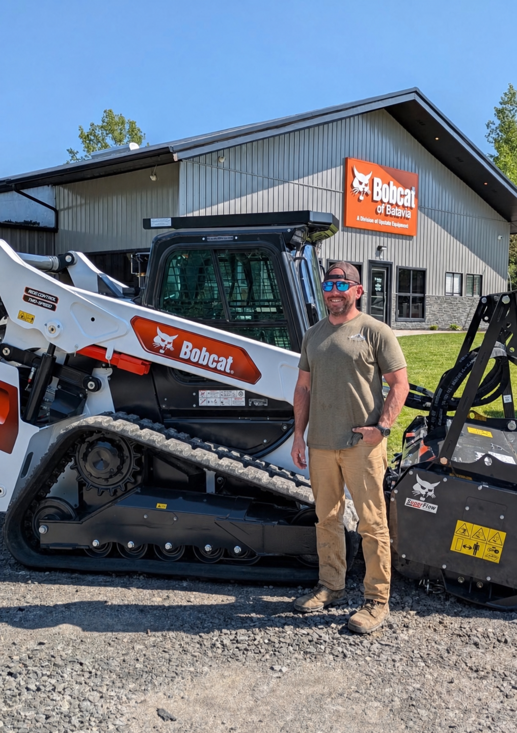 Man smiling next to a Bobcat loader outside a building with a Bobcat sign.