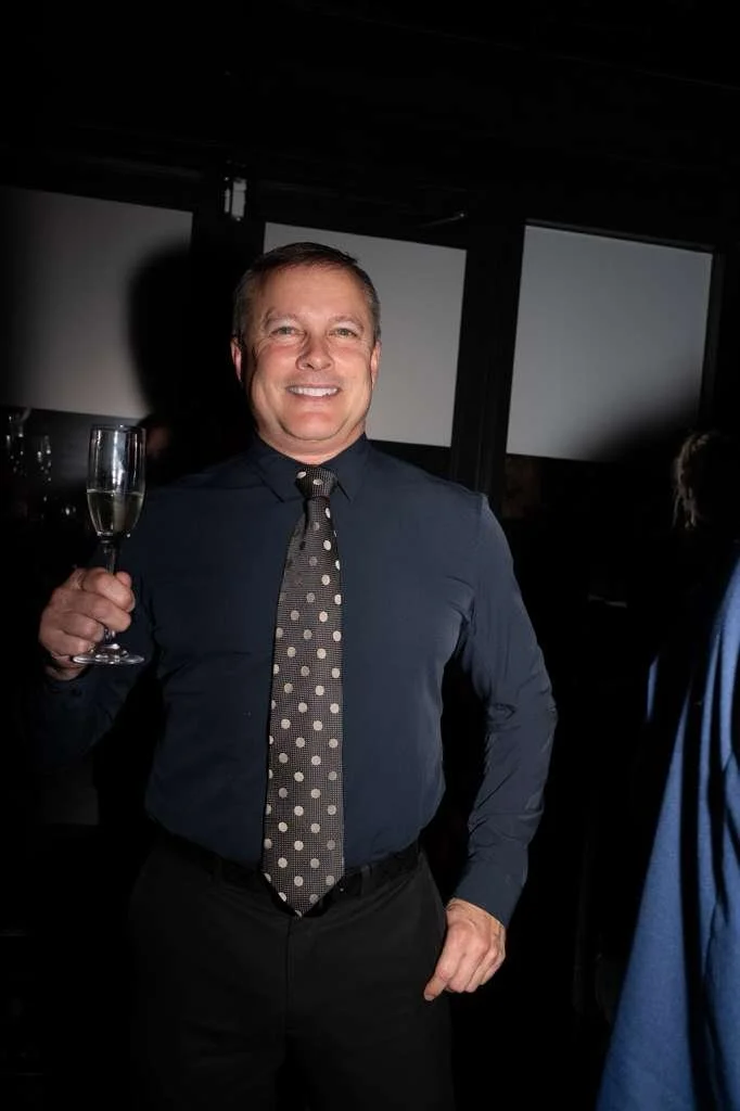 A man smiling and holding a glass of champagne at a celebration or party.