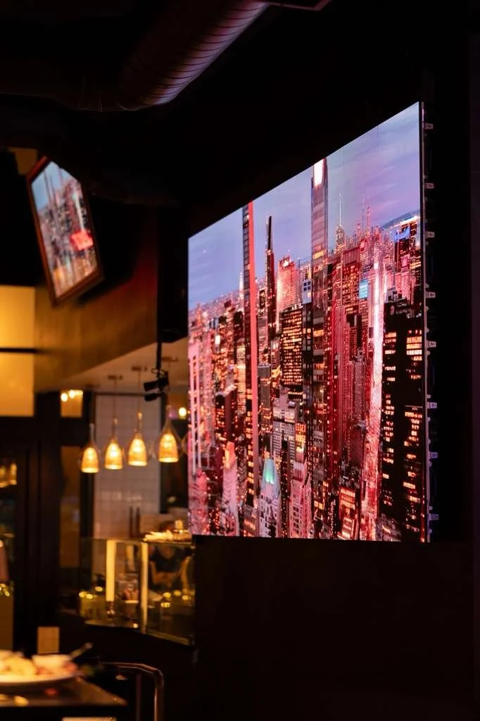 Large digital screen displaying a colorful cityscape of a downtown skyline at sunset in New York City.