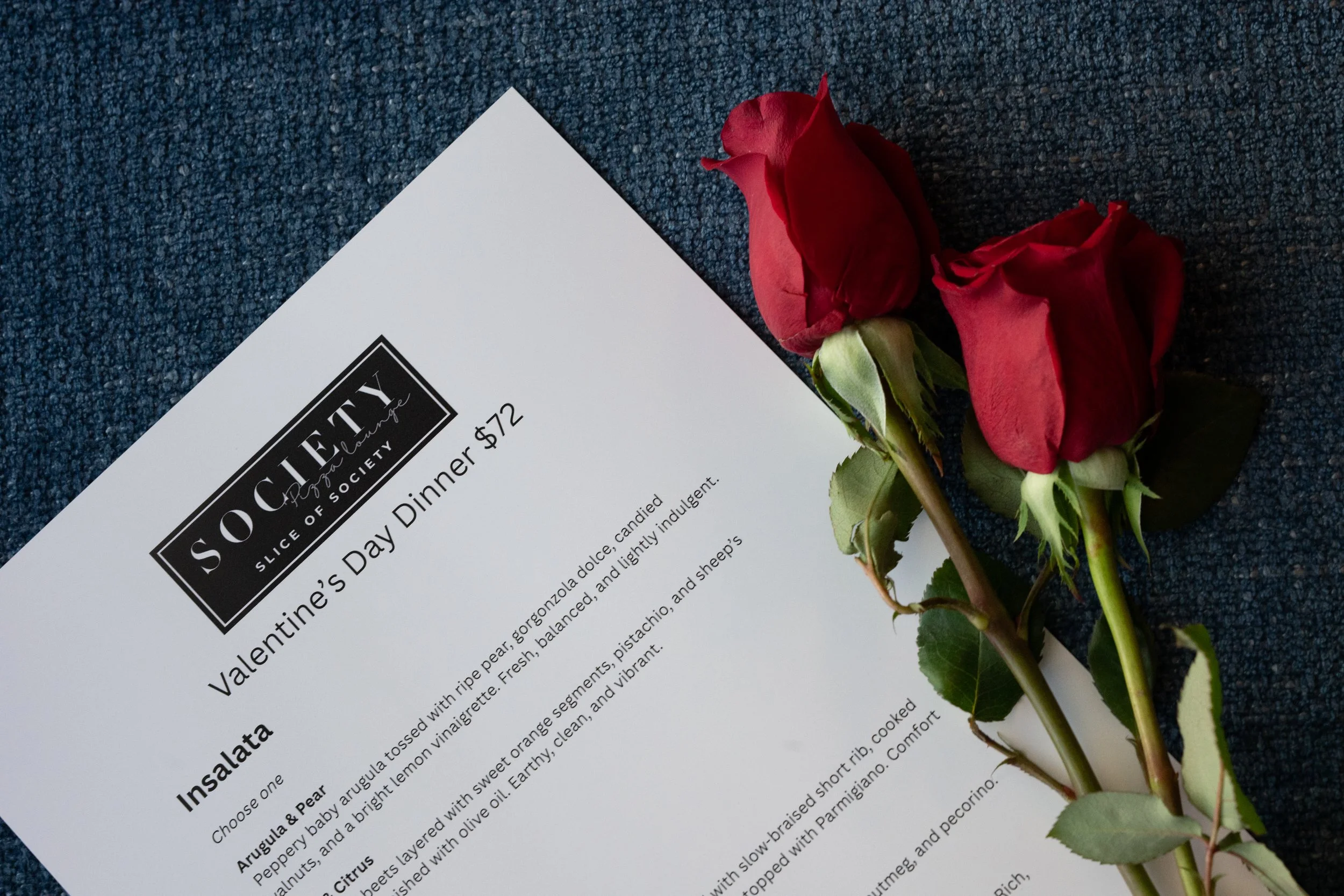 Valentine's Day dinner menu from Soho Slice of Society with two red roses on a dark textured background.