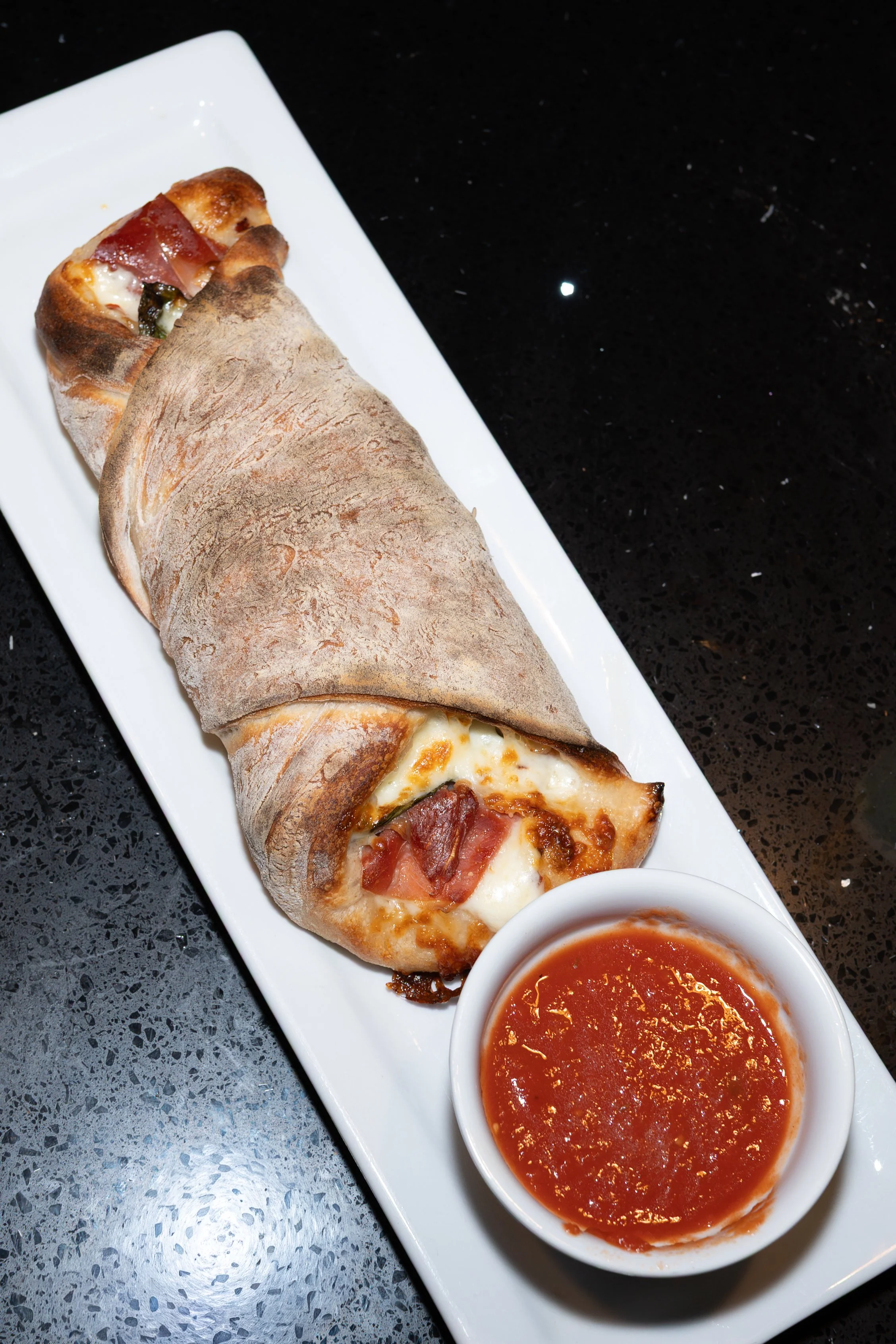A pizza roll on a long white plate with a side of marinara sauce