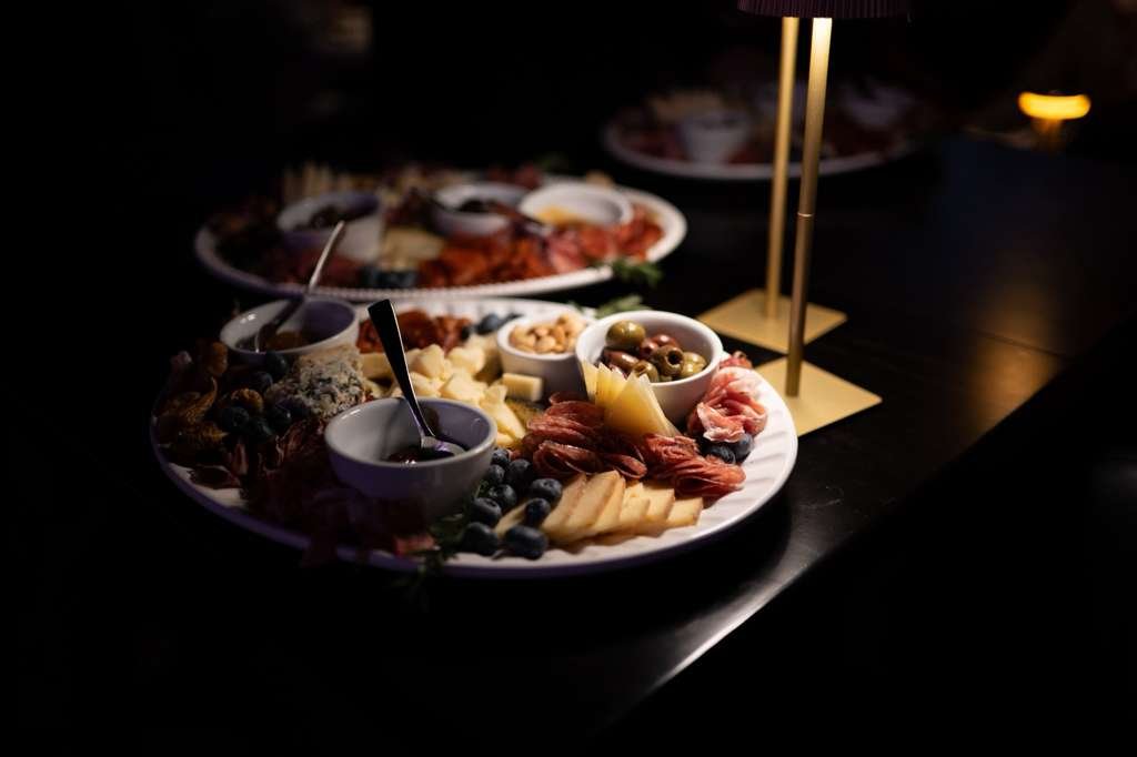 Charcuterie board with cheeses, meats, olives, blueberries, and sauces on a dark table with warm lighting.