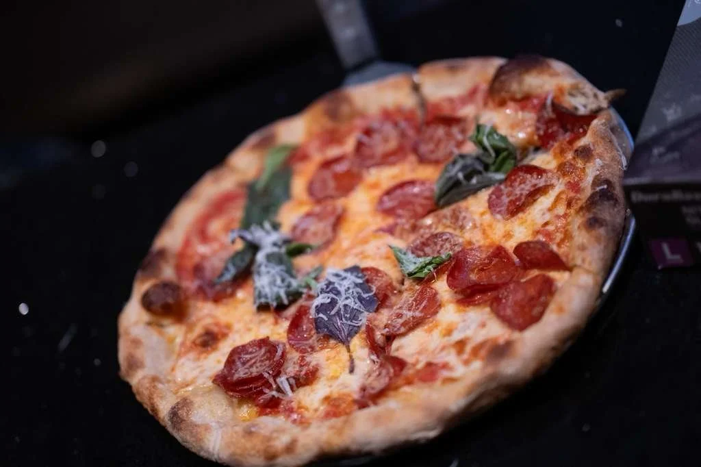 A pepperoni pizza with basil and shredded cheese resting inside a pizza box.