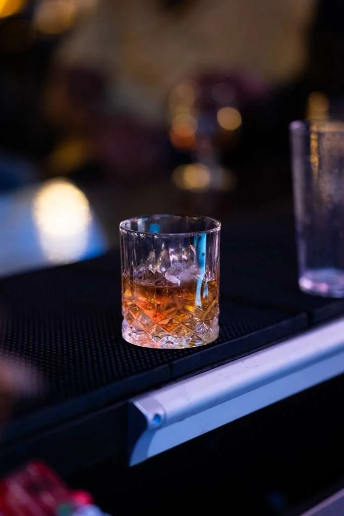 A glass of whiskey with ice on a bar counter with blurred background.