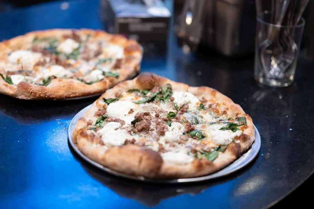 Two partially eaten pizzas with cheese, ground beef, and basil on a black table.