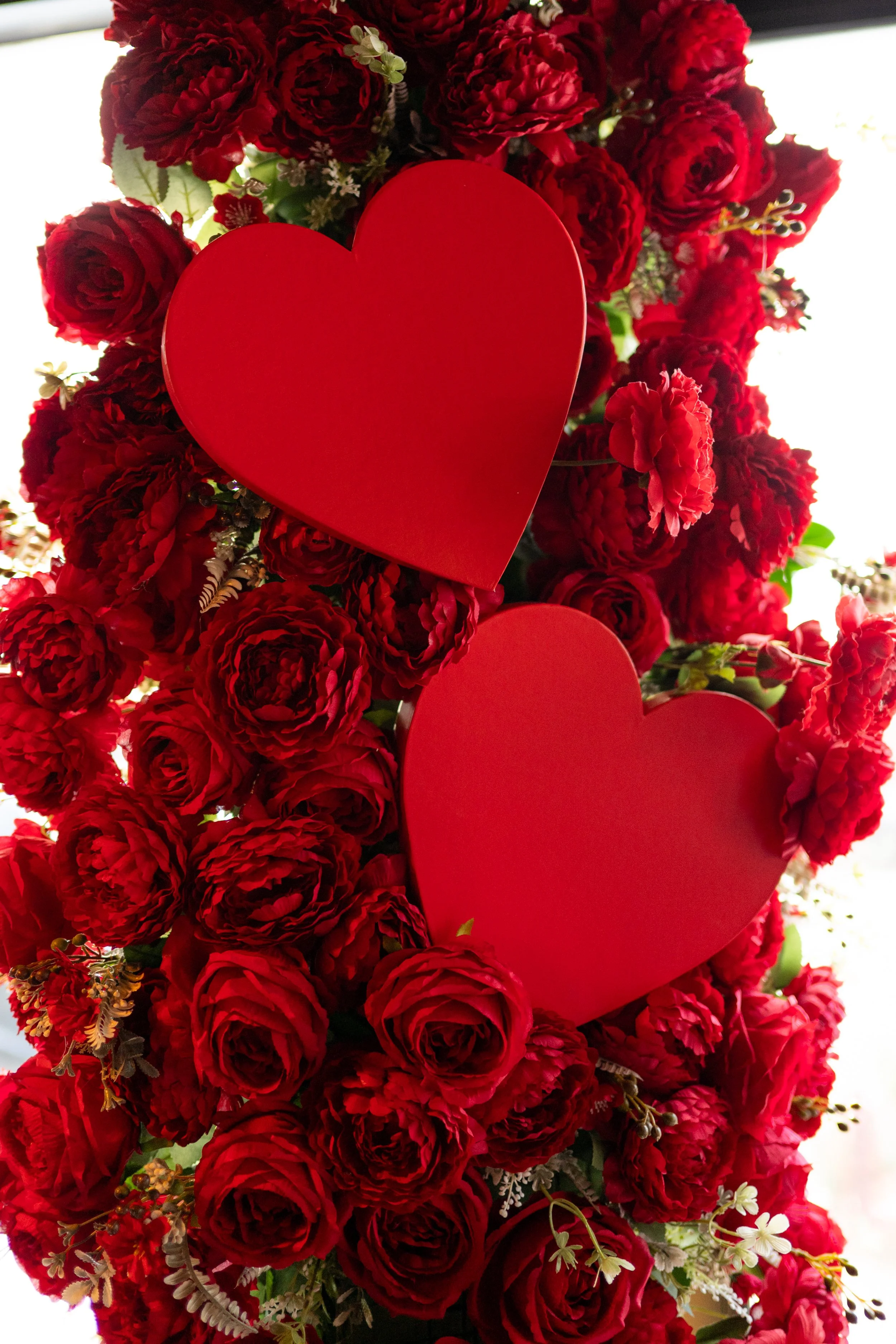 A large bouquet of red roses with two red heart decorations among the flowers.