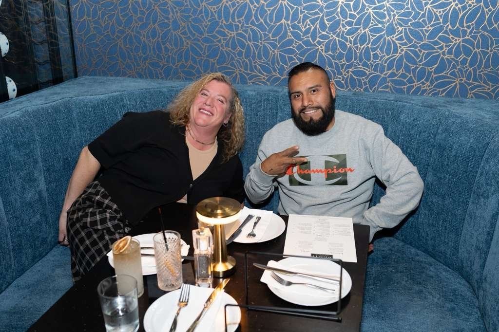 Two people sitting at a restaurant table with drink and menus, smiling and posing for the photo.