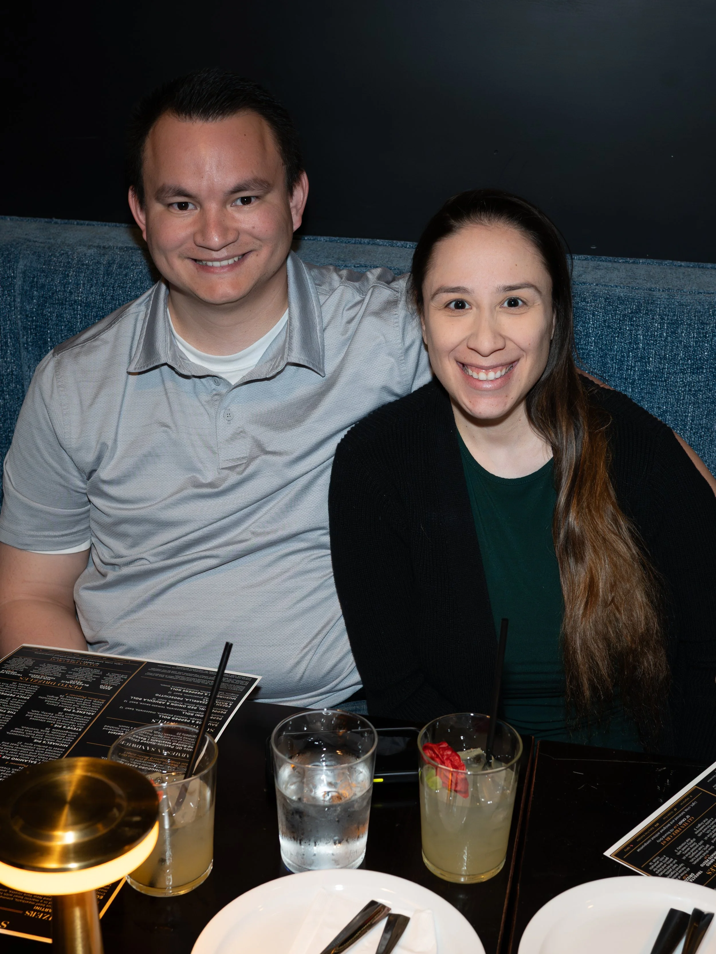 A man and woman smiling at a restaurant table with drinks, menus, and a candle.