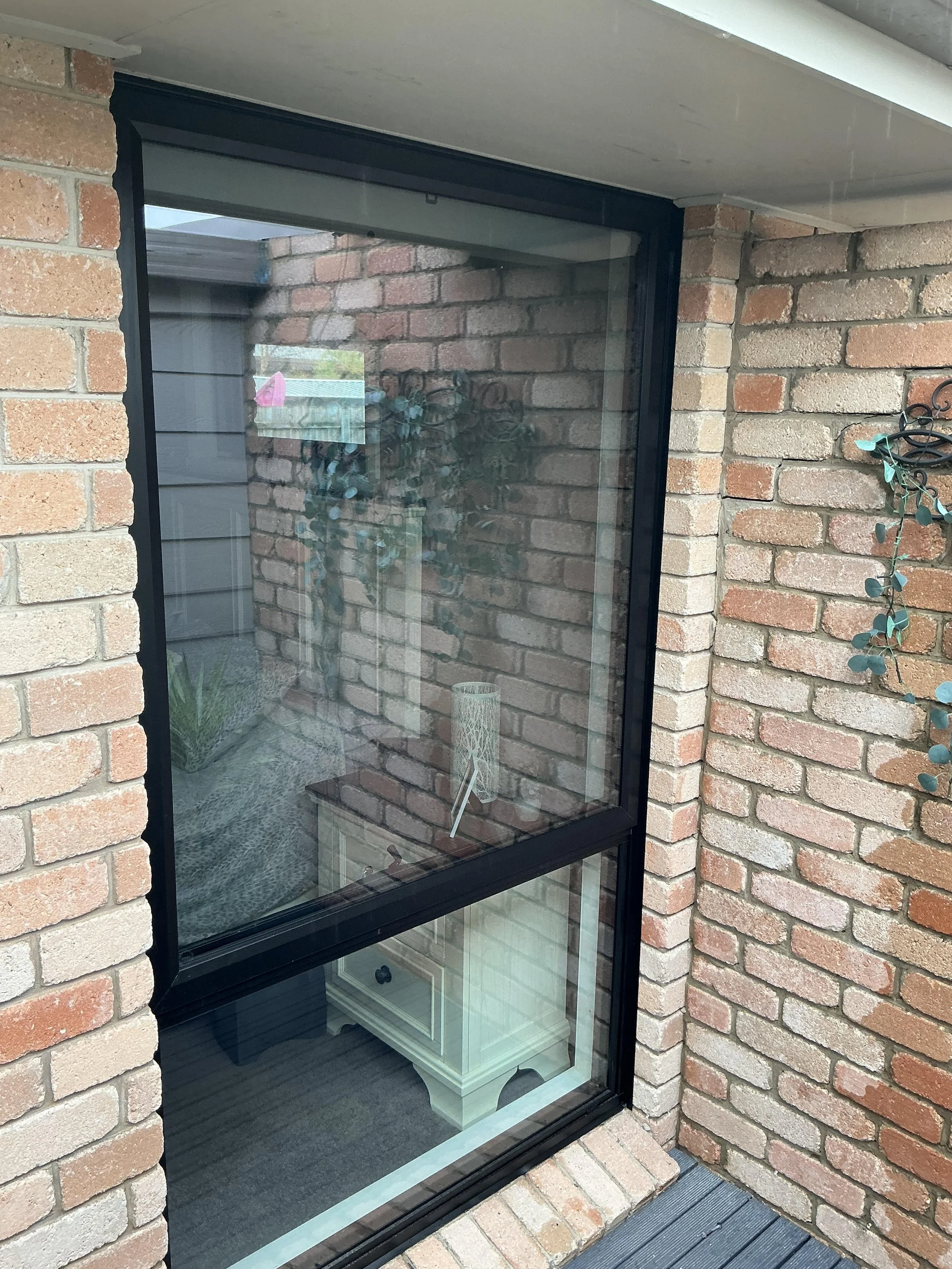 View of a screened outdoor porch area with brick walls, a glass window, and a small table with a lamp inside visible through the glass.