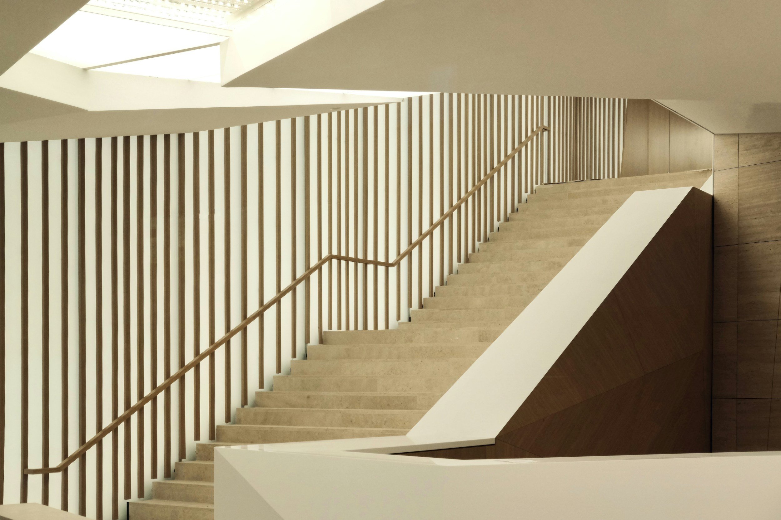 Interior view of a modern staircase with wooden railings and steps, and a geometric design with natural light coming from above.