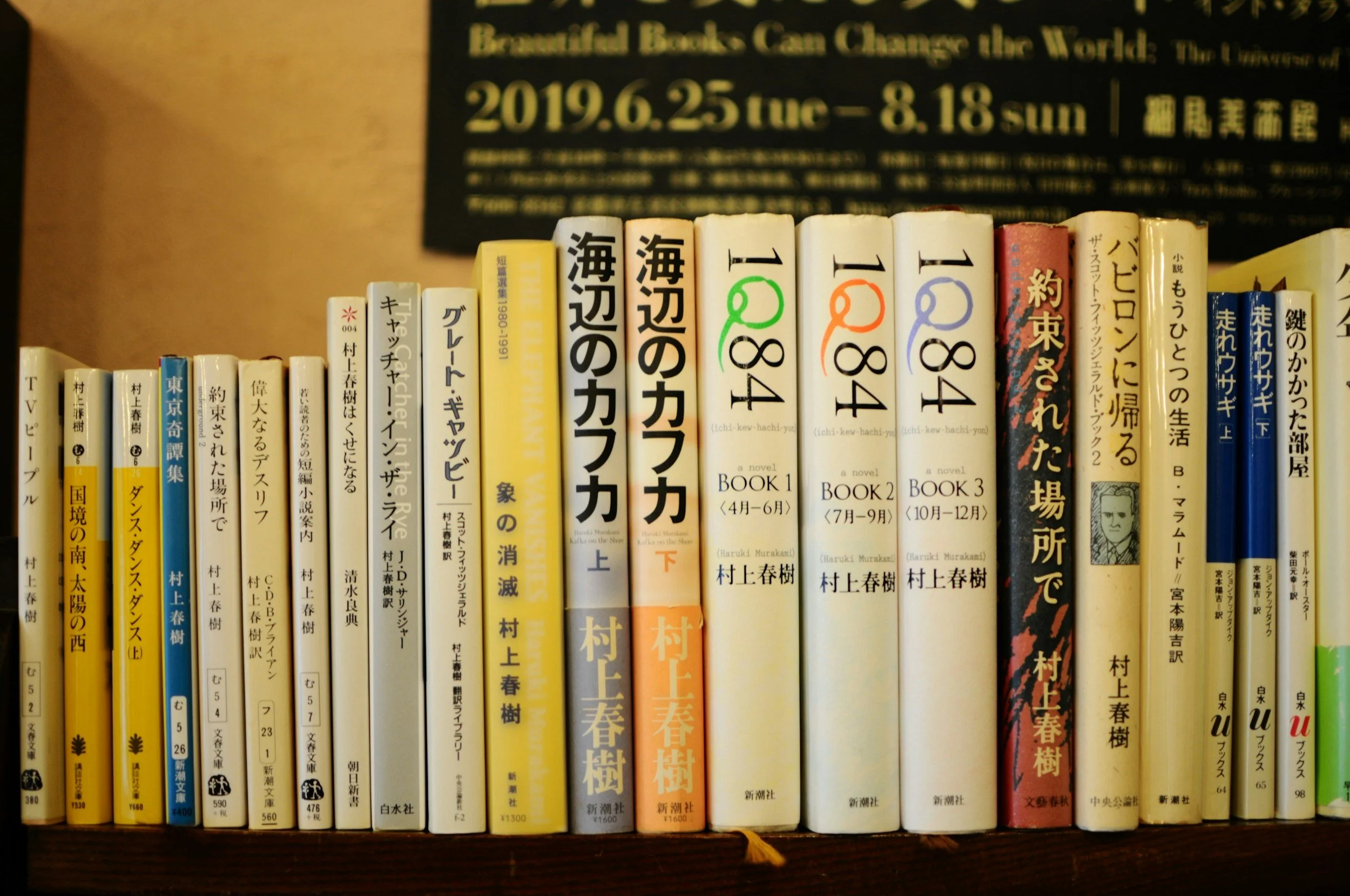 a row of Haruki Murakami's books on a bookshelf, including 1Q84, Kafka by the Sea, the Return of Babylon, and more