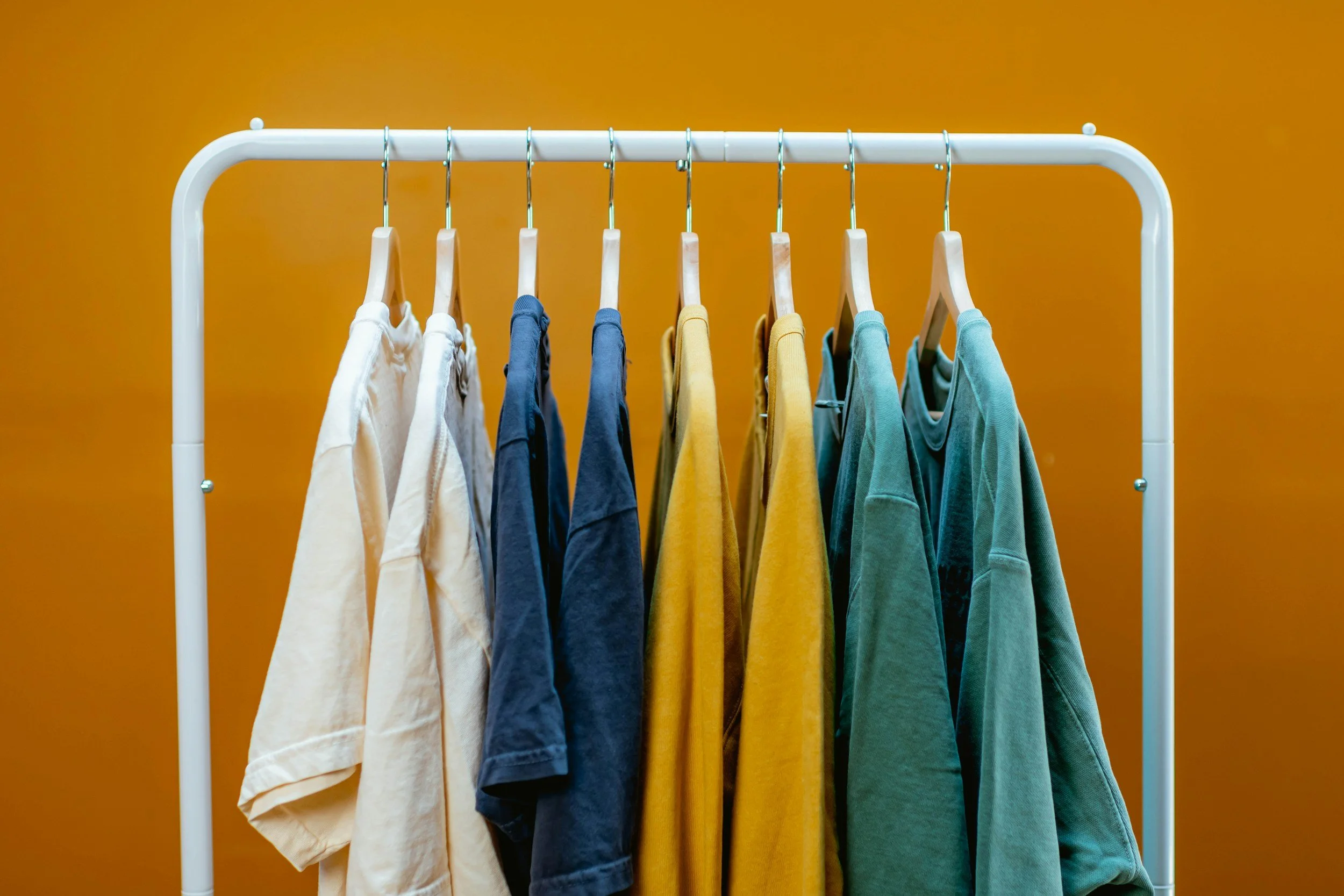 Colorful T-shirts hanging on a white clothing rack against an orange background.