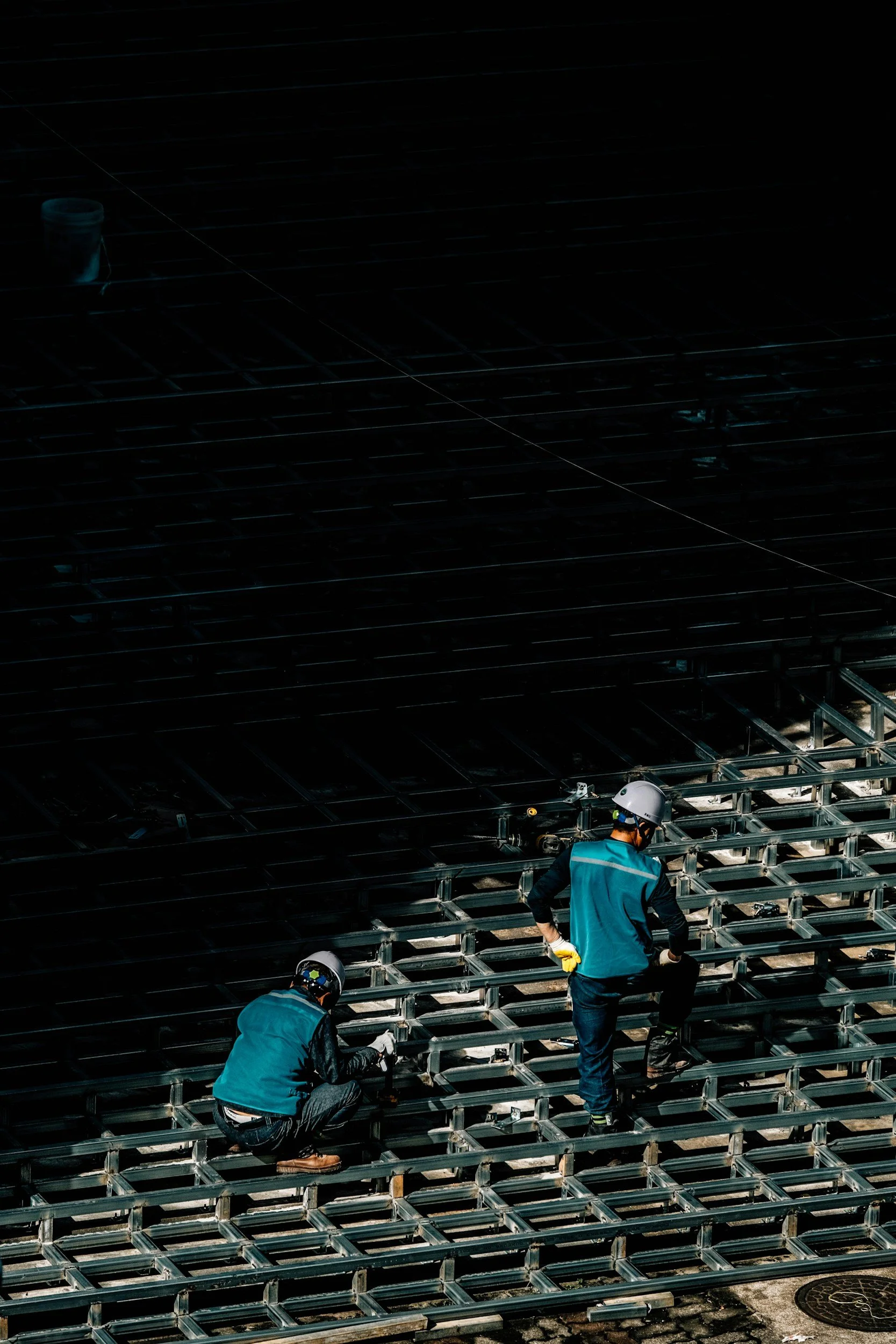 Two construction workers wearing helmets and gloves are installing metal framework on a building.