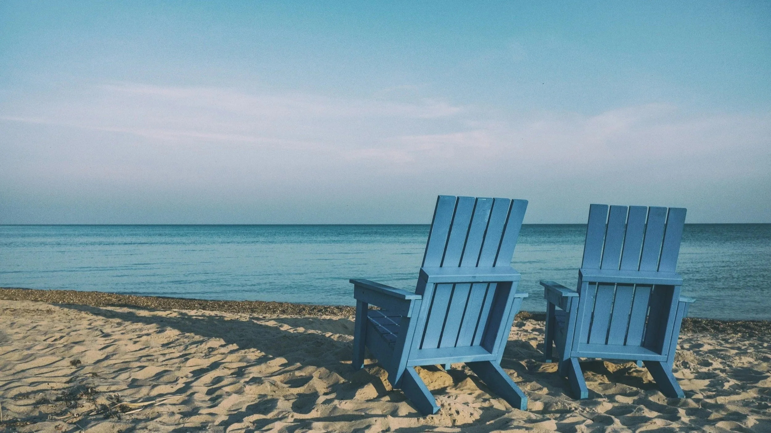 Two blue deck chairs facing a calm ocean on a quiet beach
