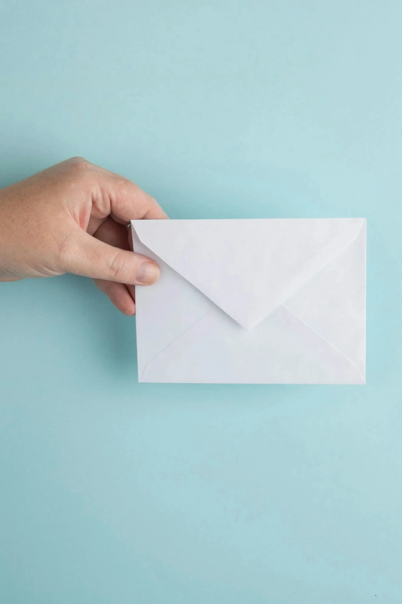 A hand holding a white folded envelope on a light blue background.