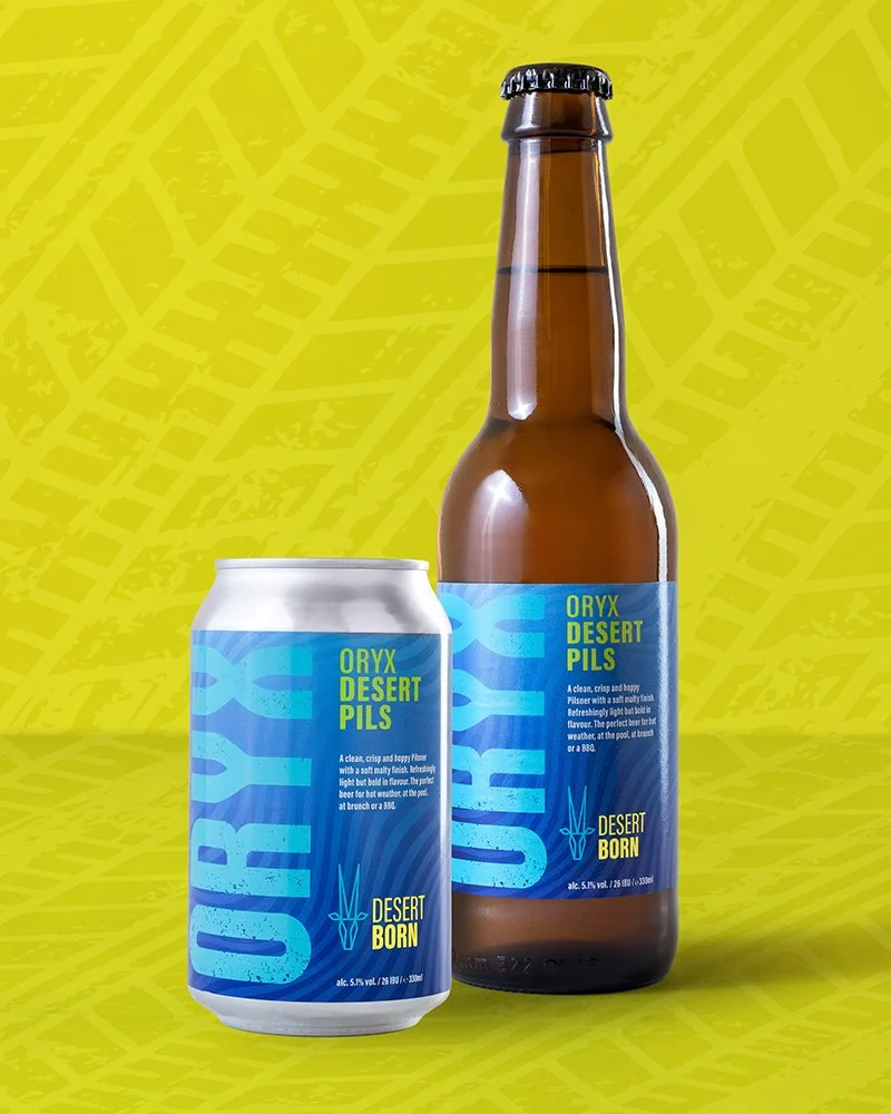 A can and a bottle of Oryx Desert Pils beer with blue labels, placed side by side against a yellow background with abstract leaf patterns.