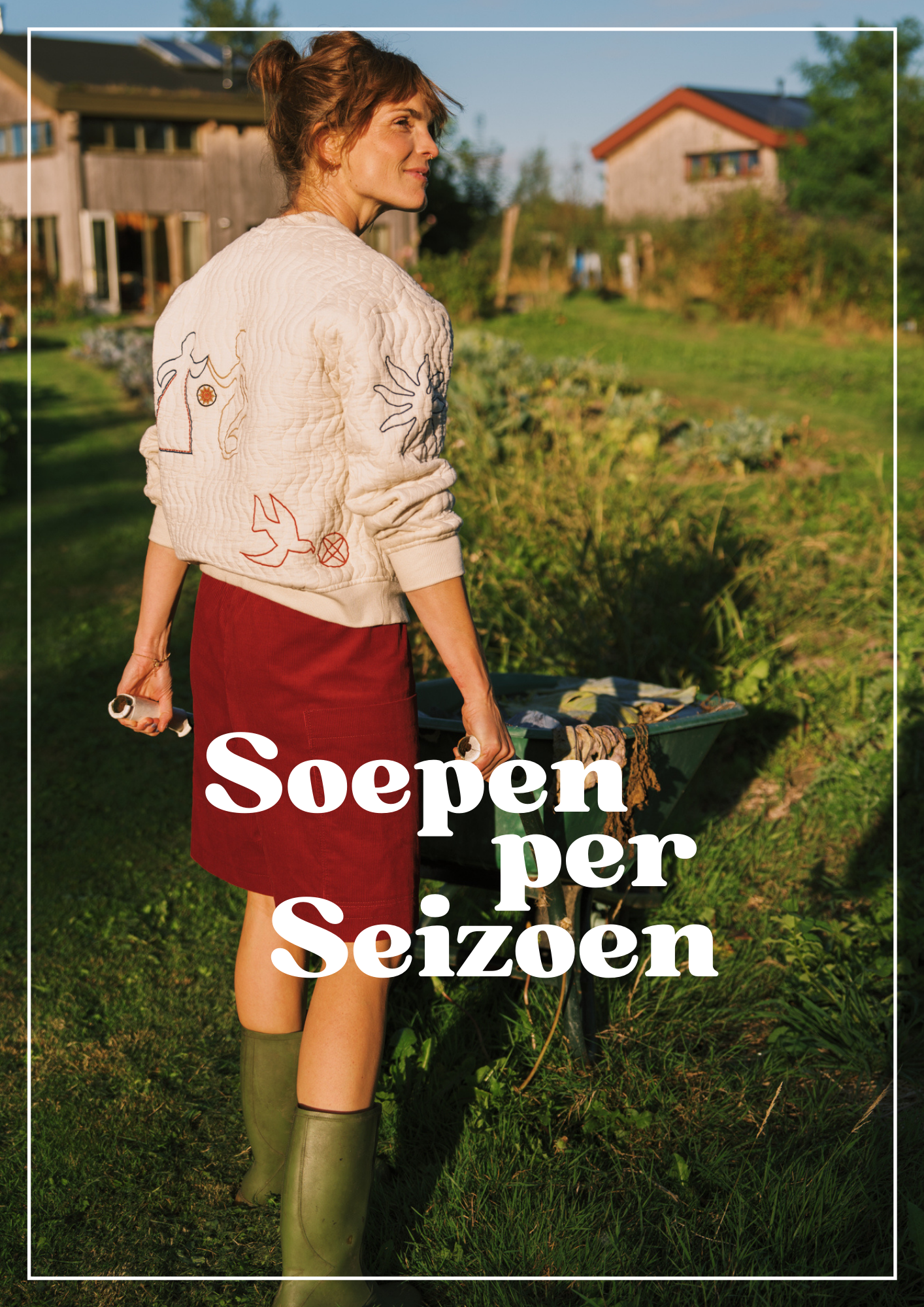 A woman with a bun hairstyle, wearing a quilted cream jacket with embroidered designs, a red skirt, and green rain boots, standing outdoors in a garden or yard with a wheelbarrow and houses in the background during late afternoon sunlight.