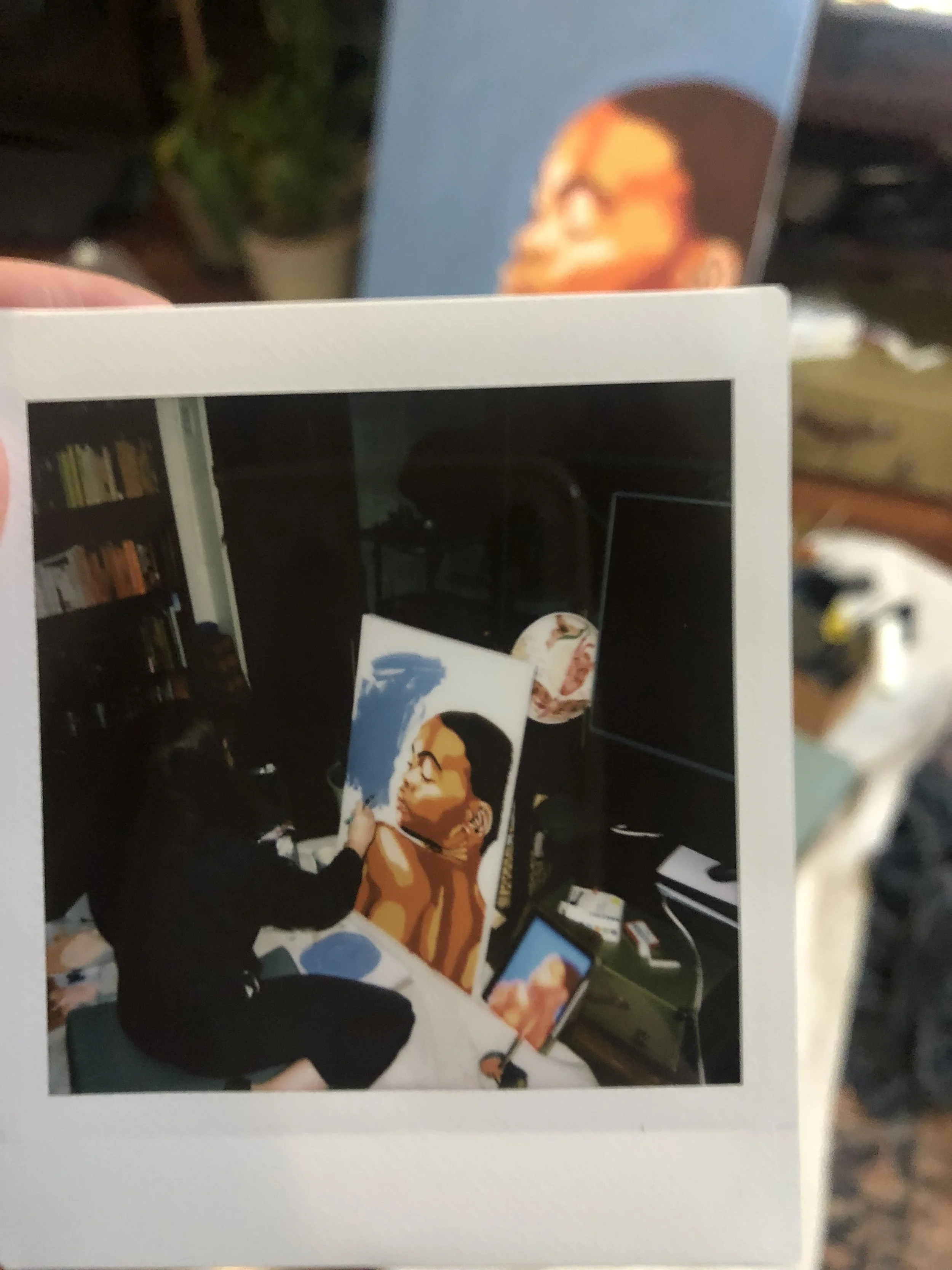 Polaroid of a person painting a portrait of a woman using an abstract style in a room filled with art supplies and books.