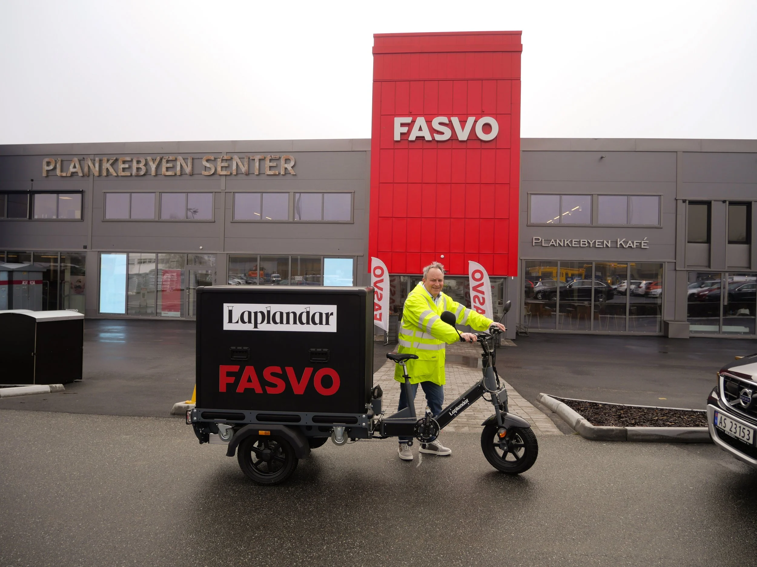 Person in yellow jacket standing with a cargo bike outside a commercial building