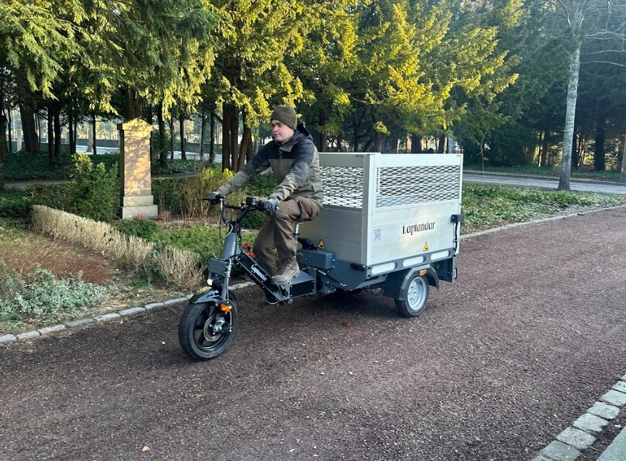 Laplandar L-250 el-arbejdscykel med transportboks i drift på smal grussti i et parkanlæg.