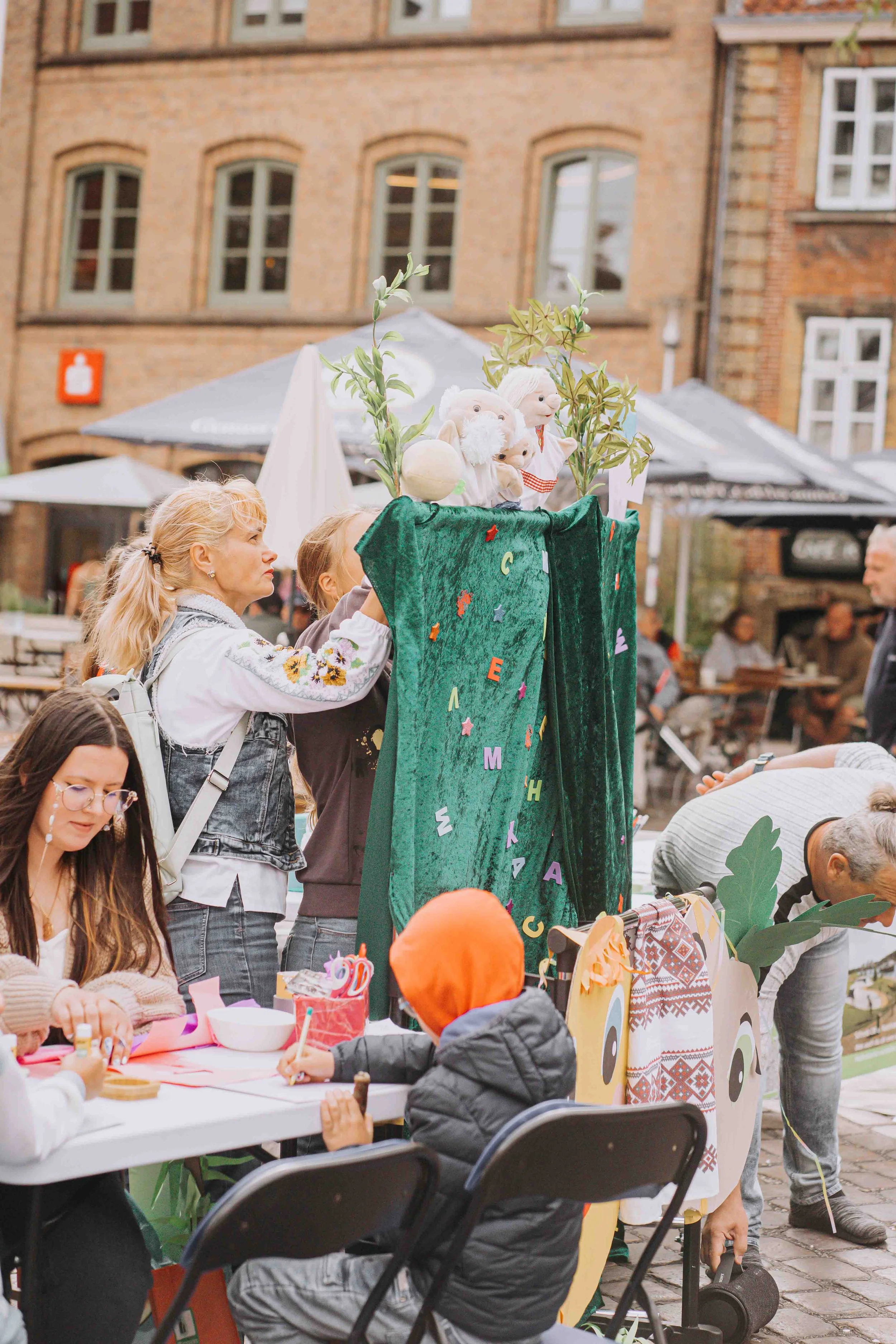 Auf dem Bild sieht man Menschen, die ein Puppentheater auf einem öffentlichen Platz spielen.
